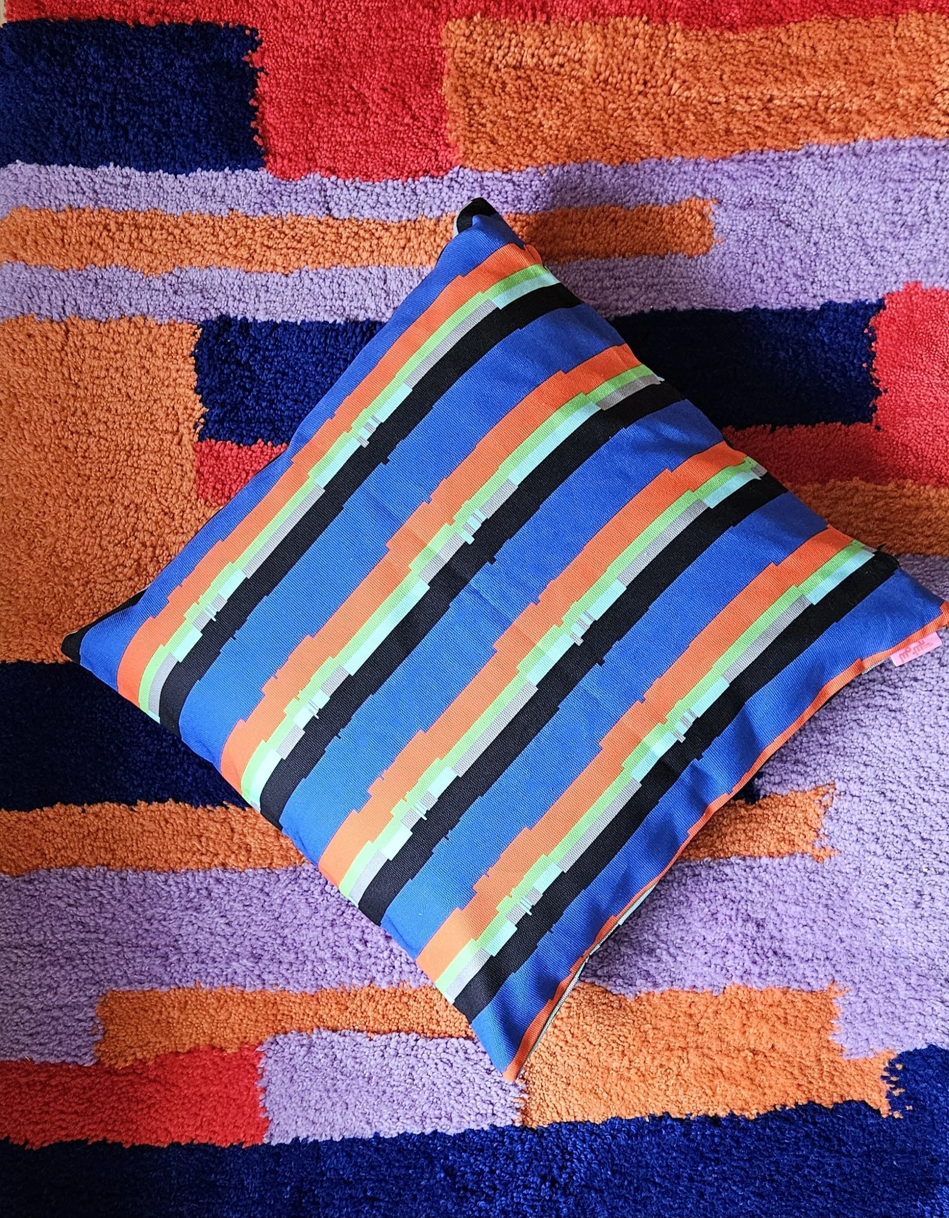 värikäs tyyny, jossa suoraviivainen kuvio, asetettuna värikkäälle, abstraktille räsymatto-taustalle.