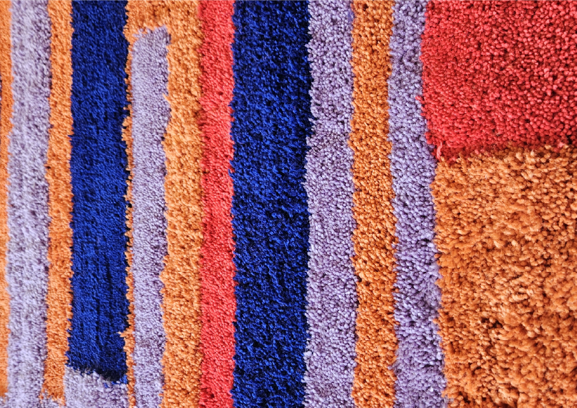 värikkäästi raidallinen matto, jossa on oranssia, punaista, sinistä ja violetin sävyjä