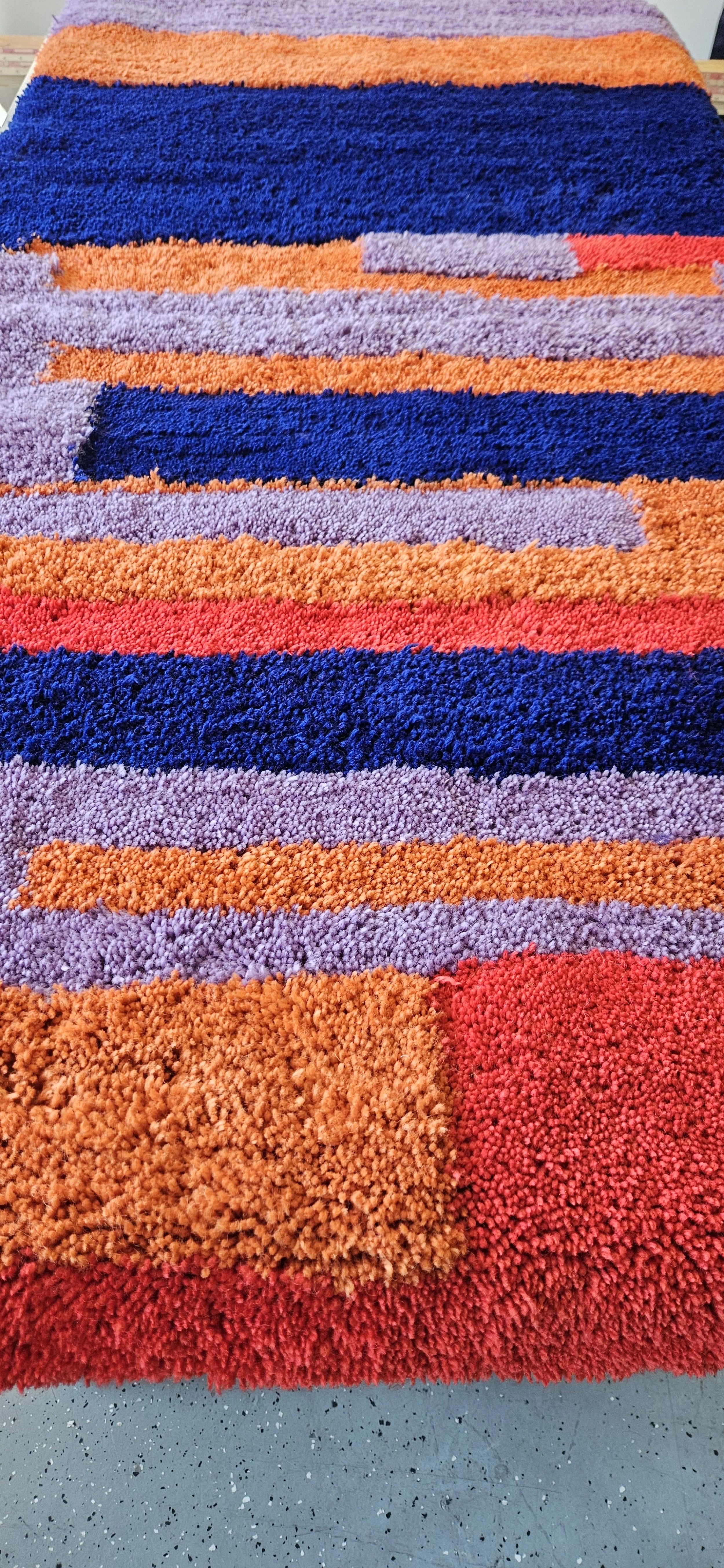 värikkäitä, raitoja ja neliöitä sisältävä paksu, pörröinen matto.