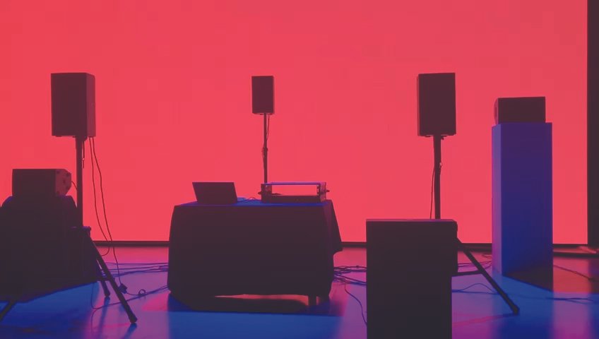 DJ-laitteet ja kaiuttimet esitystilassa, taustalla punainen seinä.