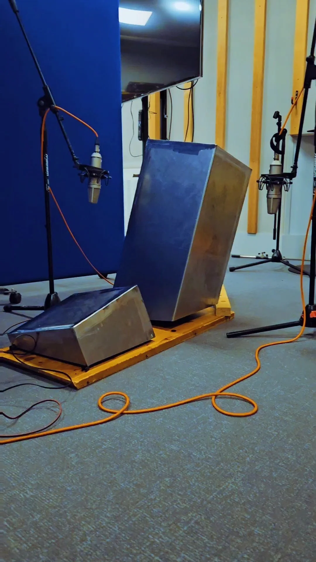 Studio-olosuhde, jossa kaksi mikrofonia ja kaksi metallipönttöä, jotka ovat alustalla, sekä äänitysstudiovaloja ja johtoja.