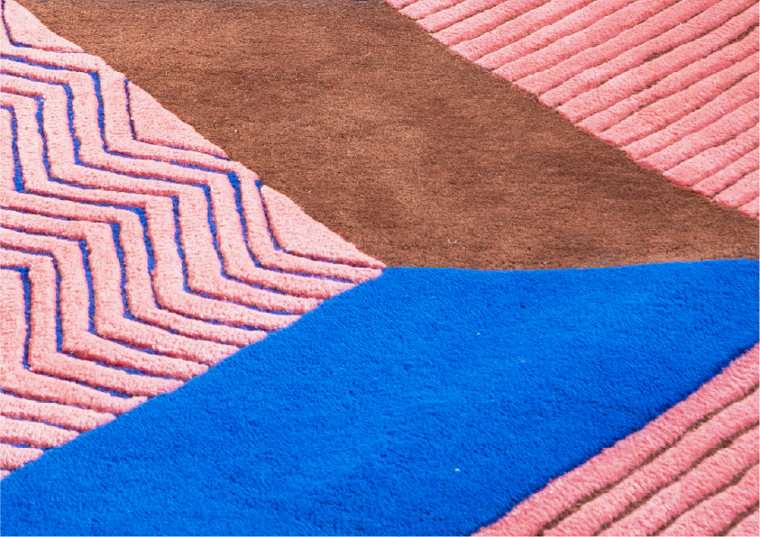 Monivärinen matto, kuvassa on pinkkiä, sinistä, ruskeaa ja vaaleanpunaista väriä, ja erilaisia geometrisia kuvioita.