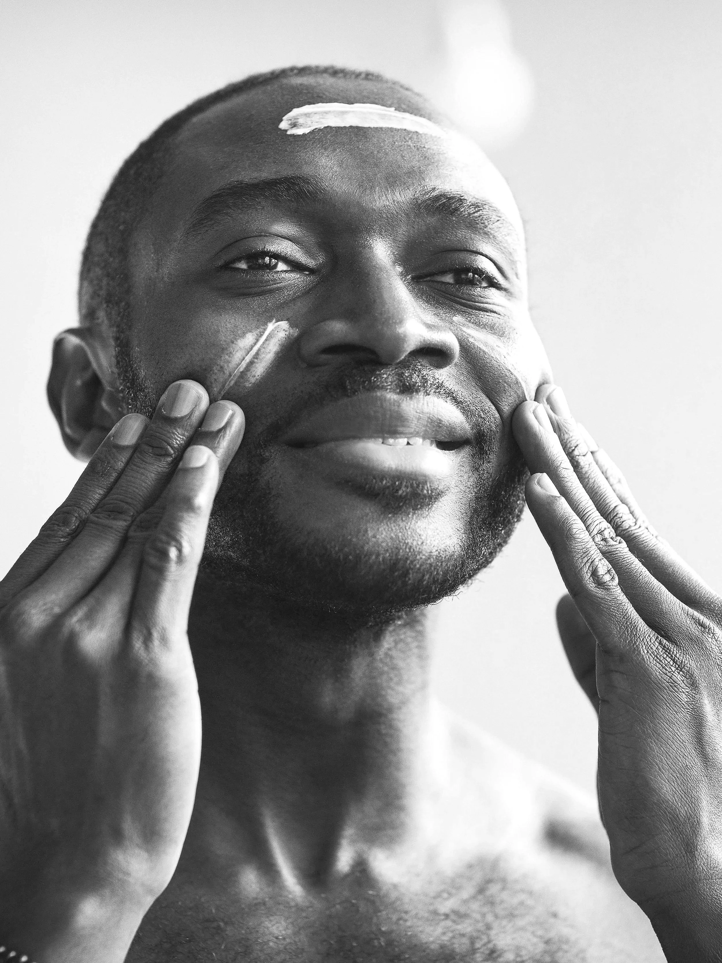 A man at HISkin, Melbourne applying skincare cream to his face, smiling, in black and white. He just had a facial and wellness treatment.