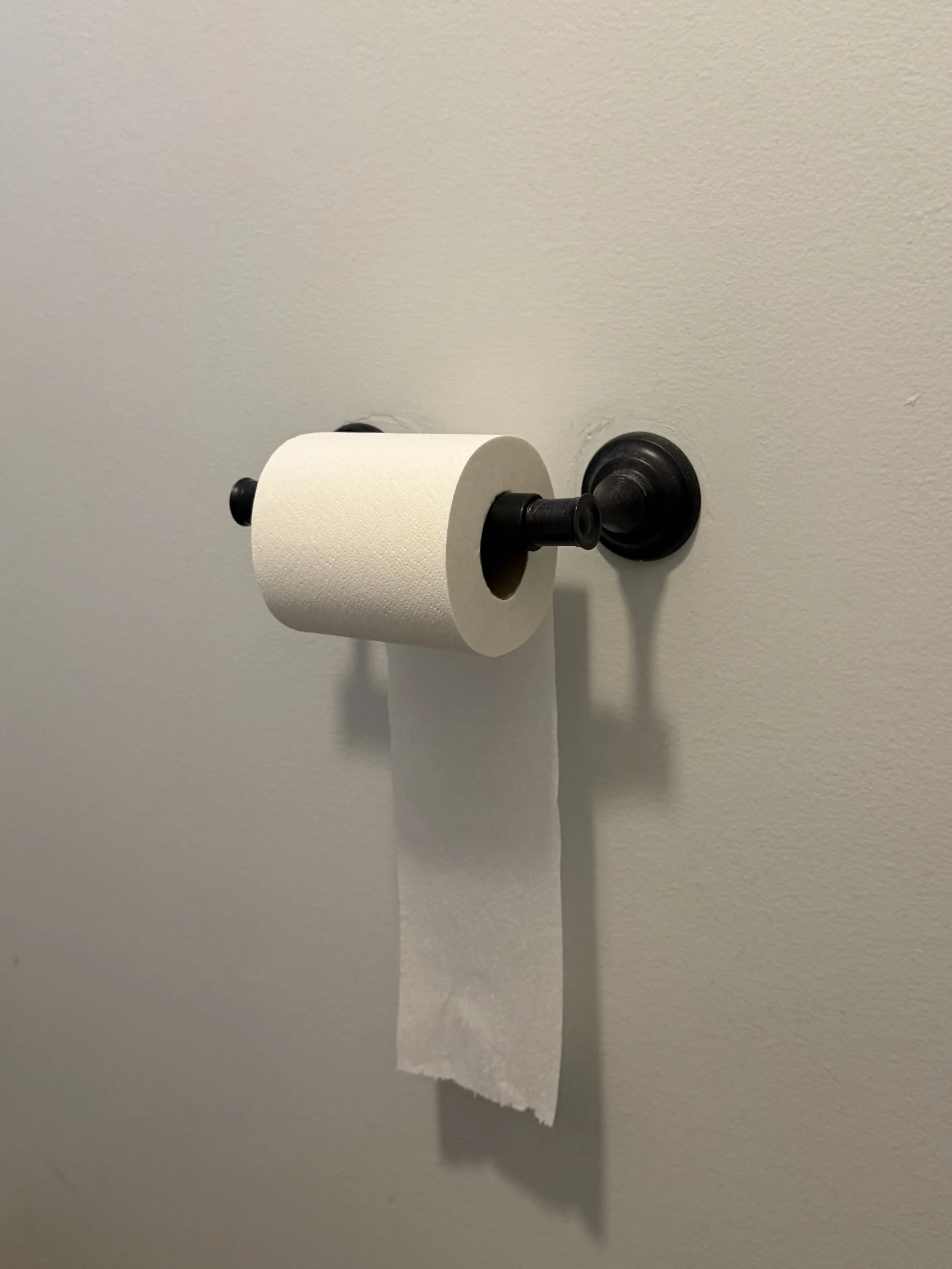 A toilet paper roll mounted on a wall with a piece of toilet paper hanging down.