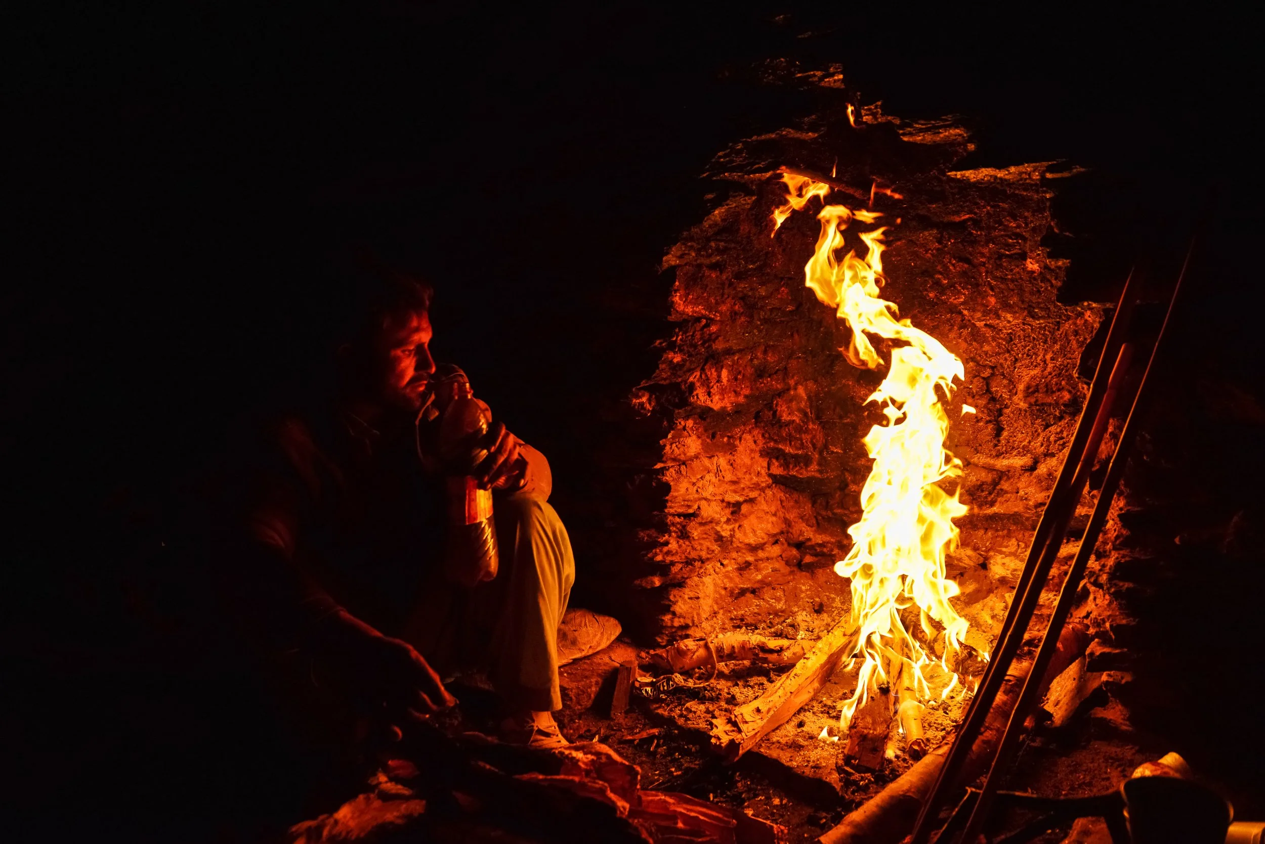 A person sitting near a campfire at night, illuminated by the fire's glow.