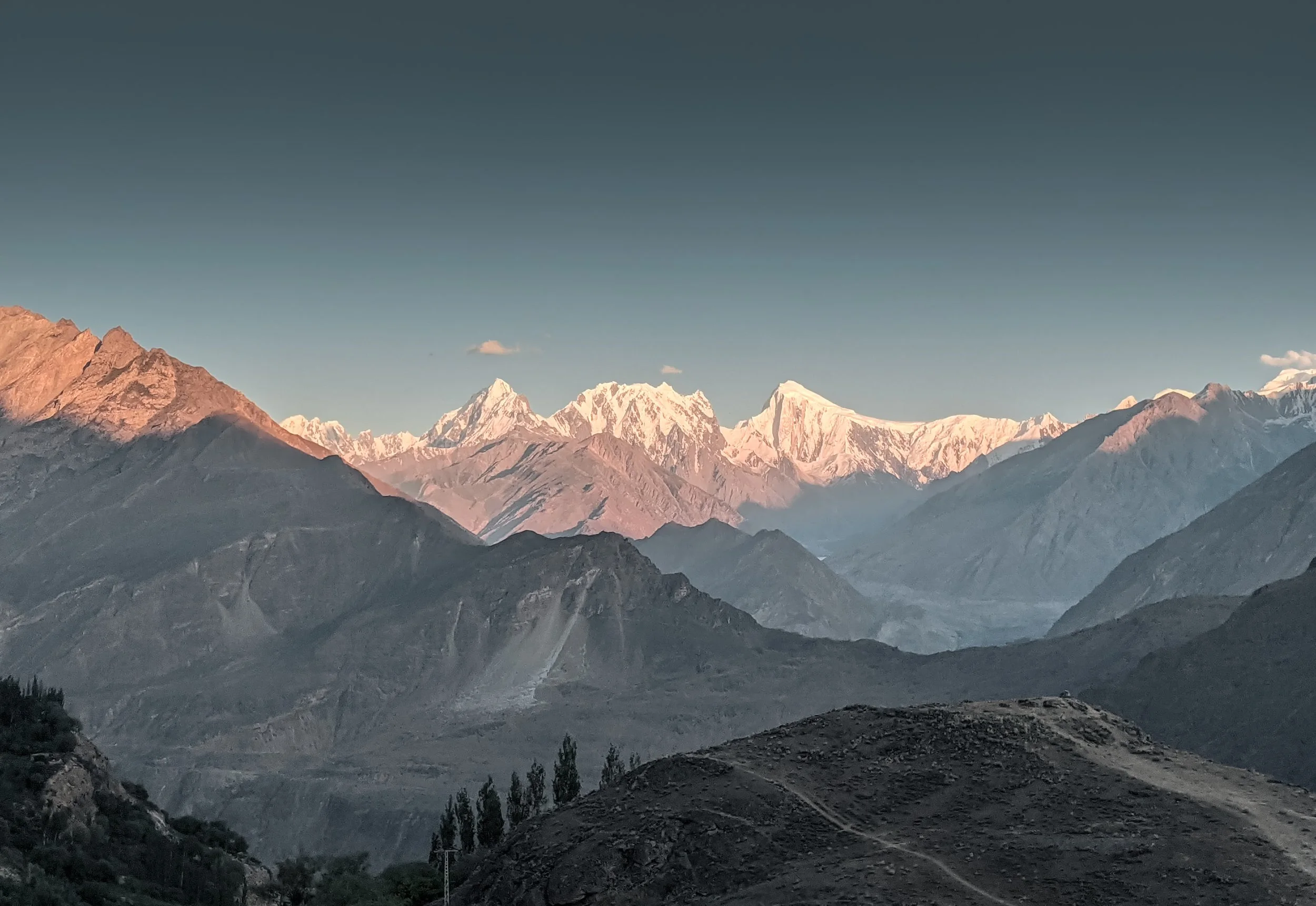 Snow-capped mountains in the distance with rugged, rocky terrain in the foreground under a clear sky.