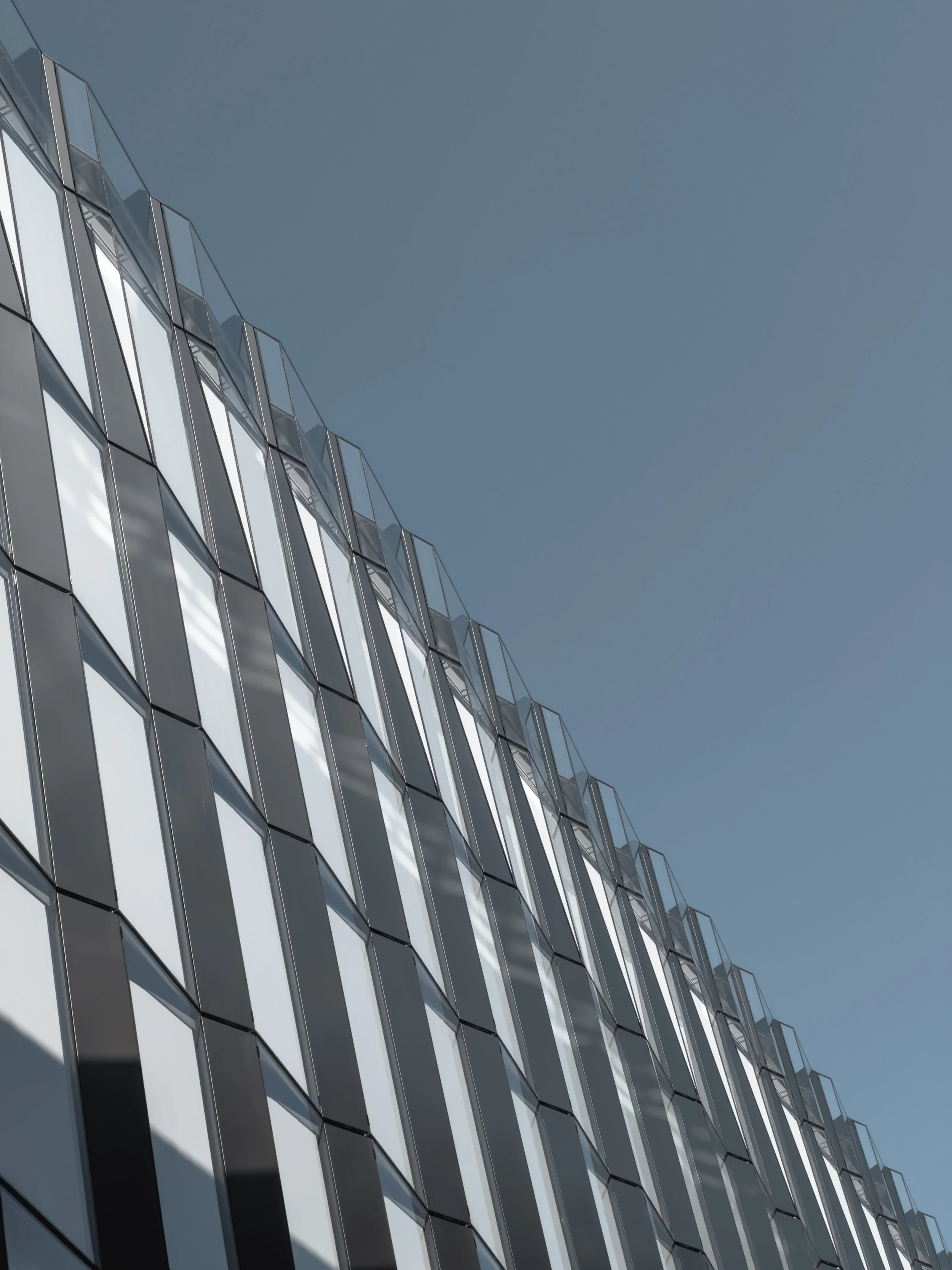 Modern building with glass facade seen from below against a clear blue sky.