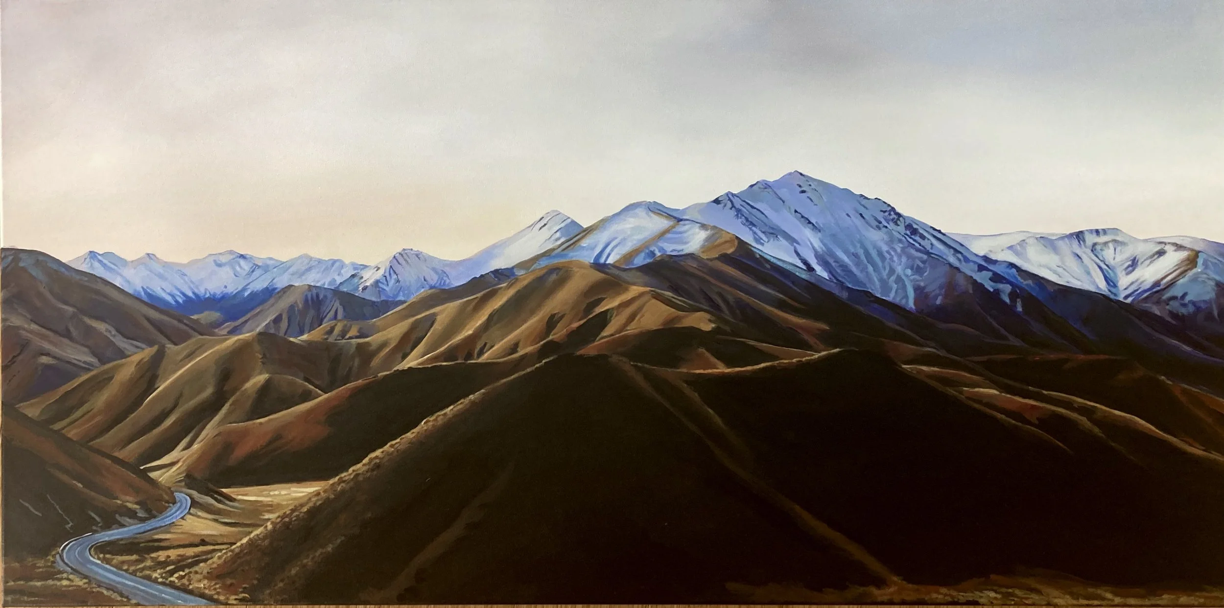 Painted landscape of mountain ranges with snow-capped peaks in the background and brown, rolling hills in the foreground. A winding road is seen cutting through the hills.