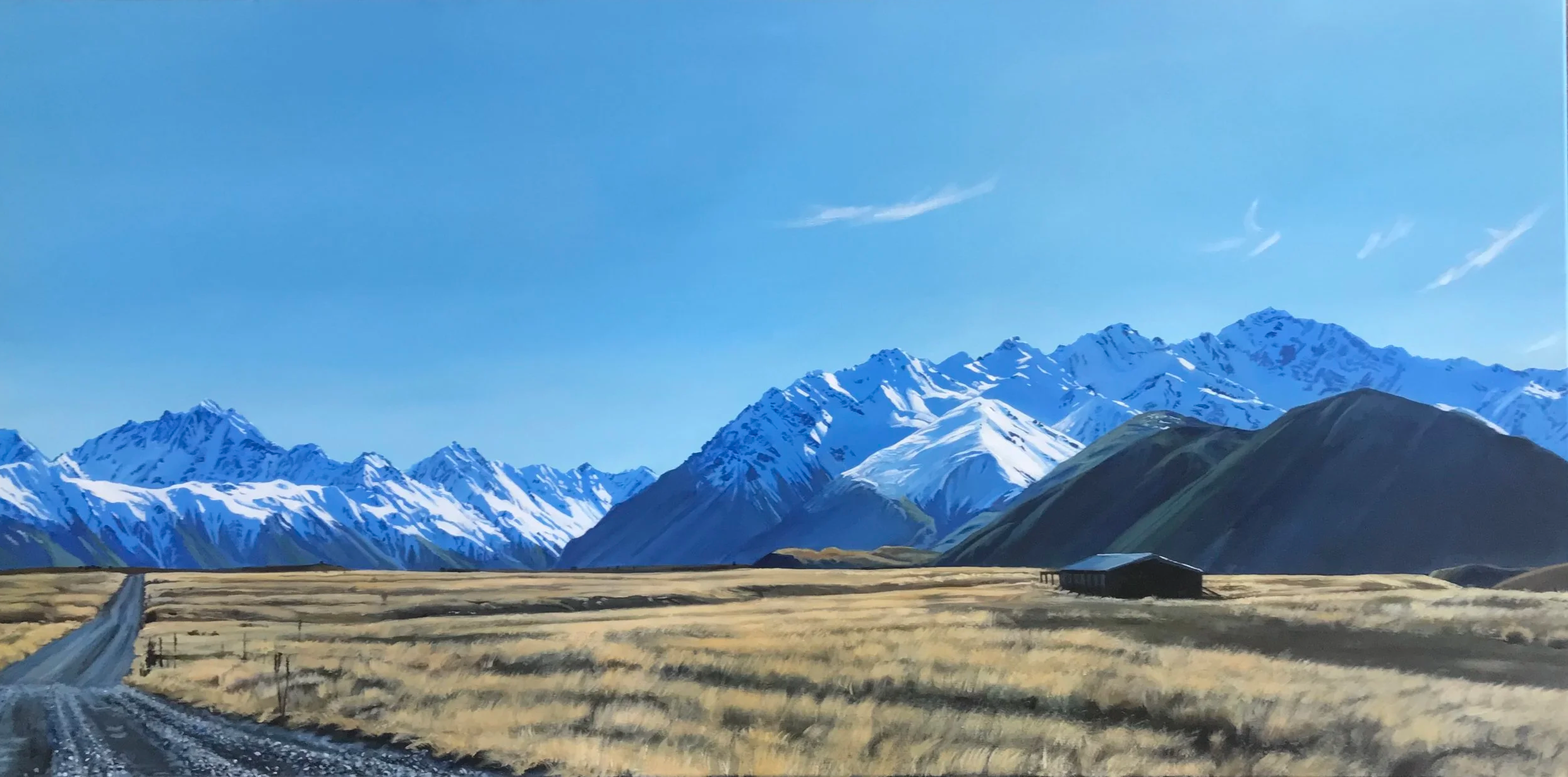 Snow-capped mountains under a blue sky, a dirt road, and a barn in a grassy field.