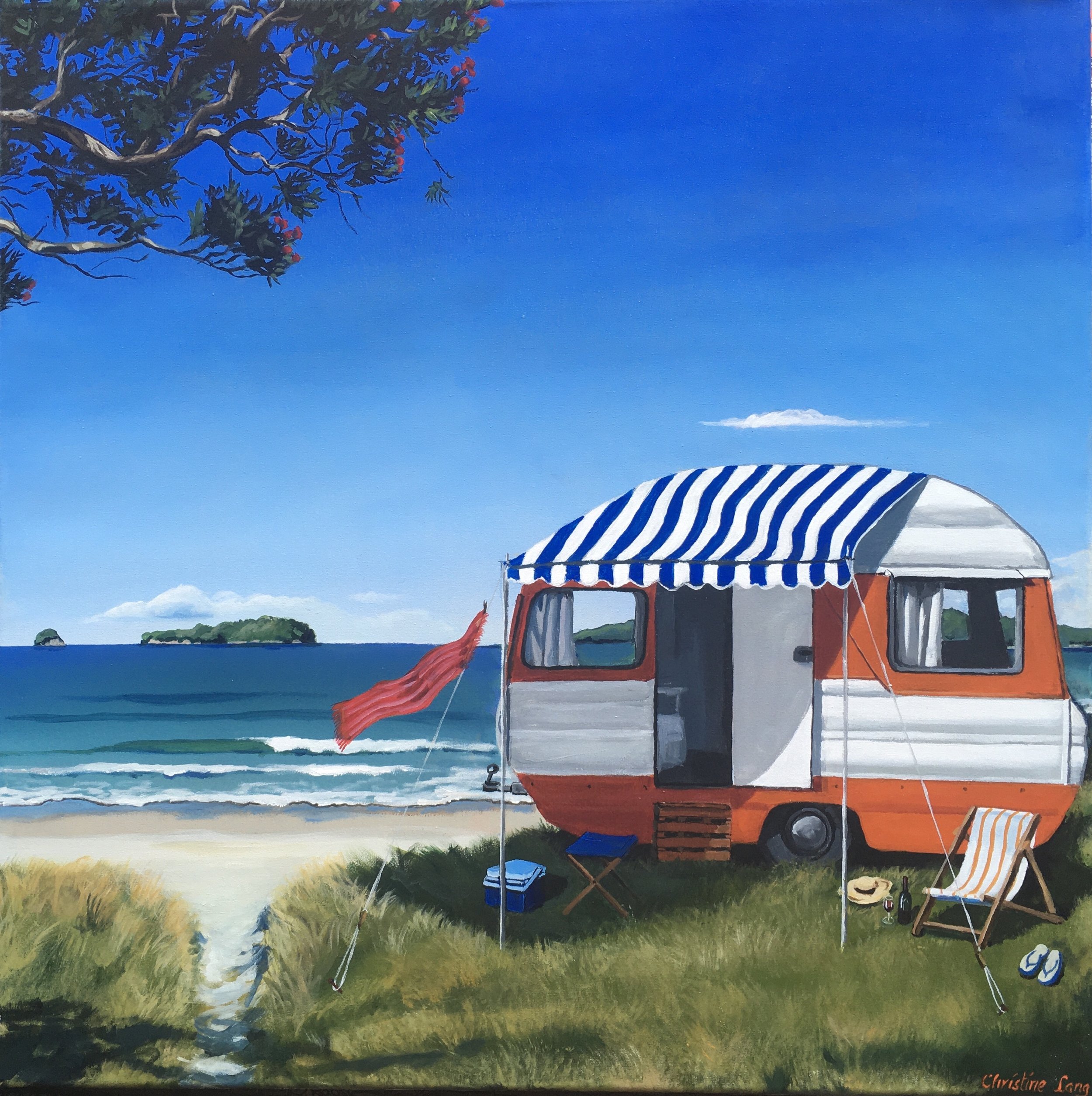 A vintage camper trailer with a blue and white striped awning parked on a grassy area near the beach, with chairs and a cooler outside, overlooking the ocean with small islands in the distance under a clear blue sky.