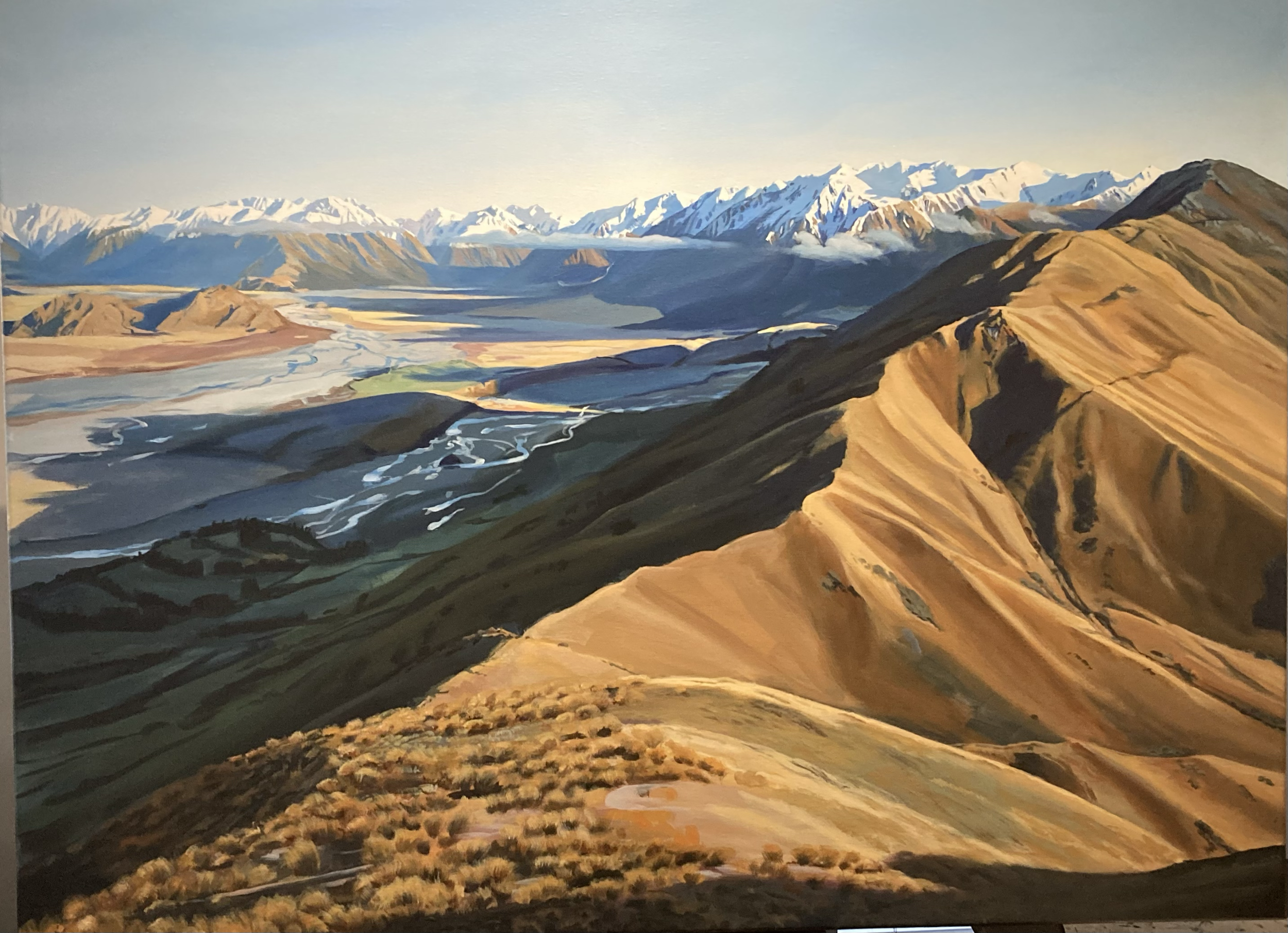 A landscape painting of mountains, valleys, and rivers with snow-capped peaks in the distance, green and brown rolling hills in the foreground, and a clear sky.