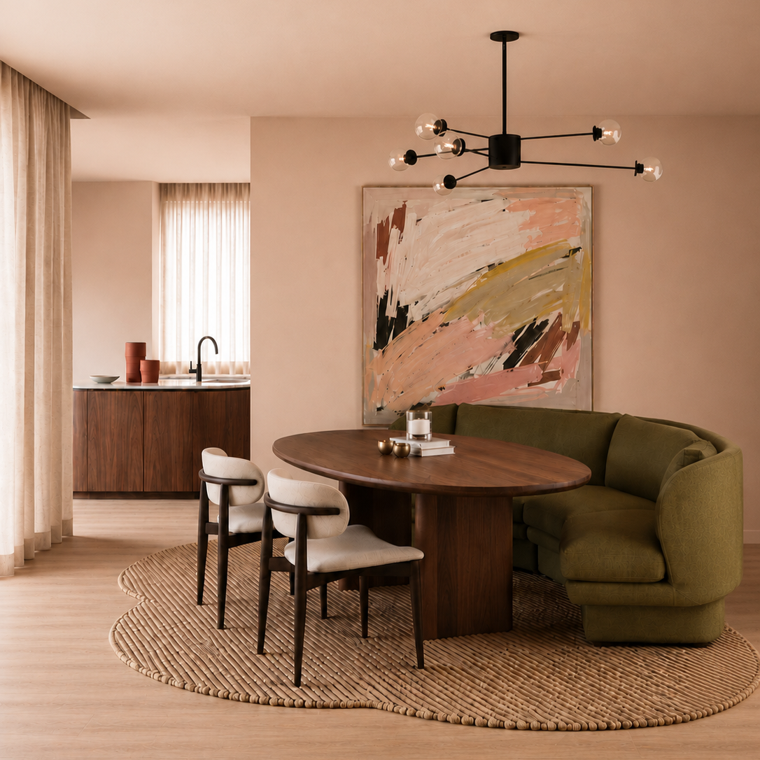 Modern dining room with a round wooden table, green sectional sofa, abstract wall art, and a black chandelier with exposed bulbs. Light wood flooring with a round woven rug, nearby kitchen with beige curtains, wooden cabinets, and a window.