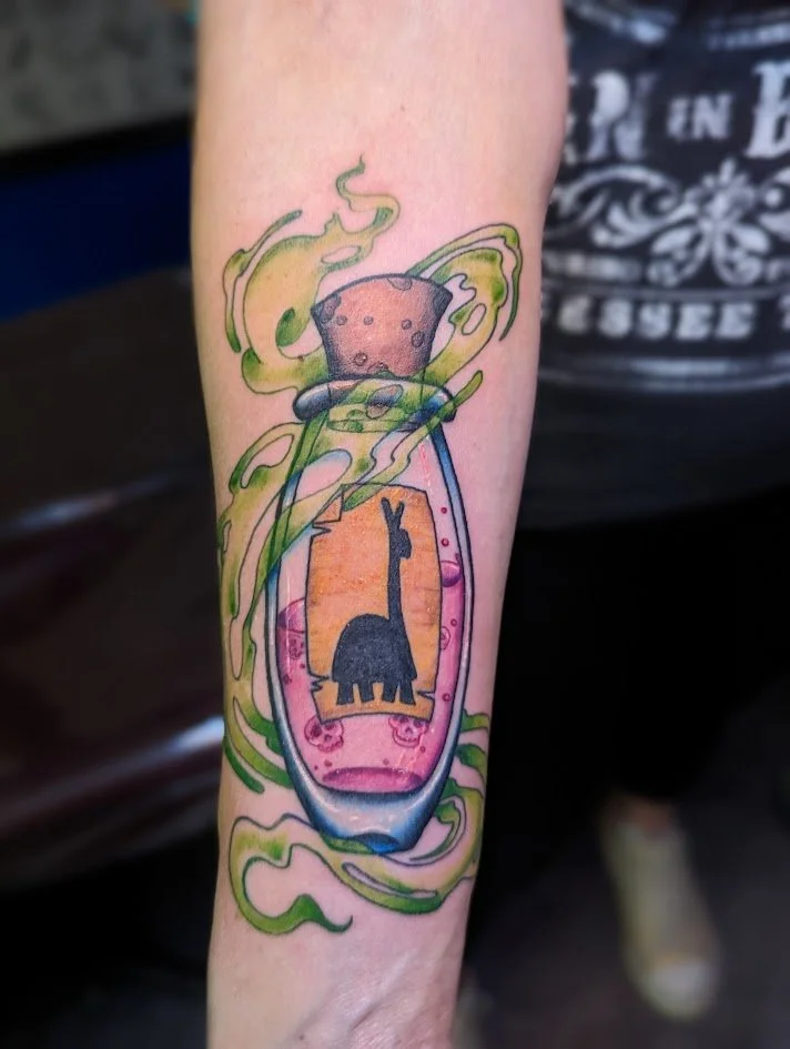 Colorful tattoo of a smashed bottle with a silhouette of a giraffe inside, surrounded by green swirling lines and sparks.
