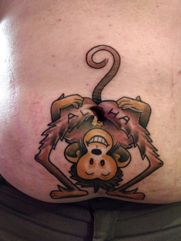 Tattoo of a cartoon monkey hanging upside down with arms behind its head, smiling, with the words 'PLAY HARD' written across its chest.