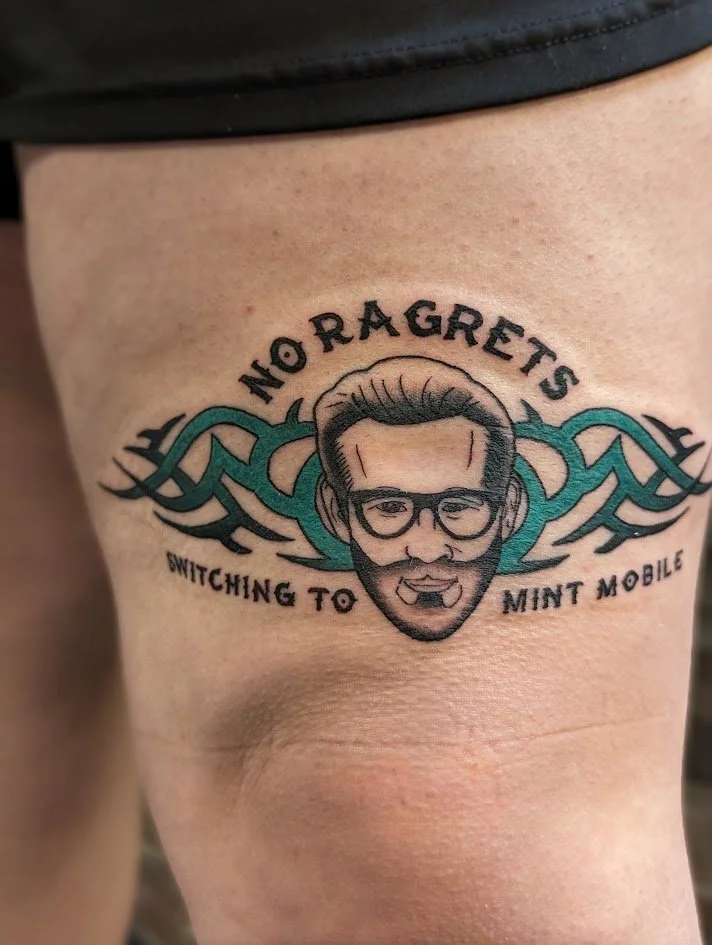 Tattoo of a man's face with glasses, mustache, and goatee, with the text "NO RAGRETS" above and "SWITCHING TO MINT MOBILE" below, and a teal tribal design in the background.