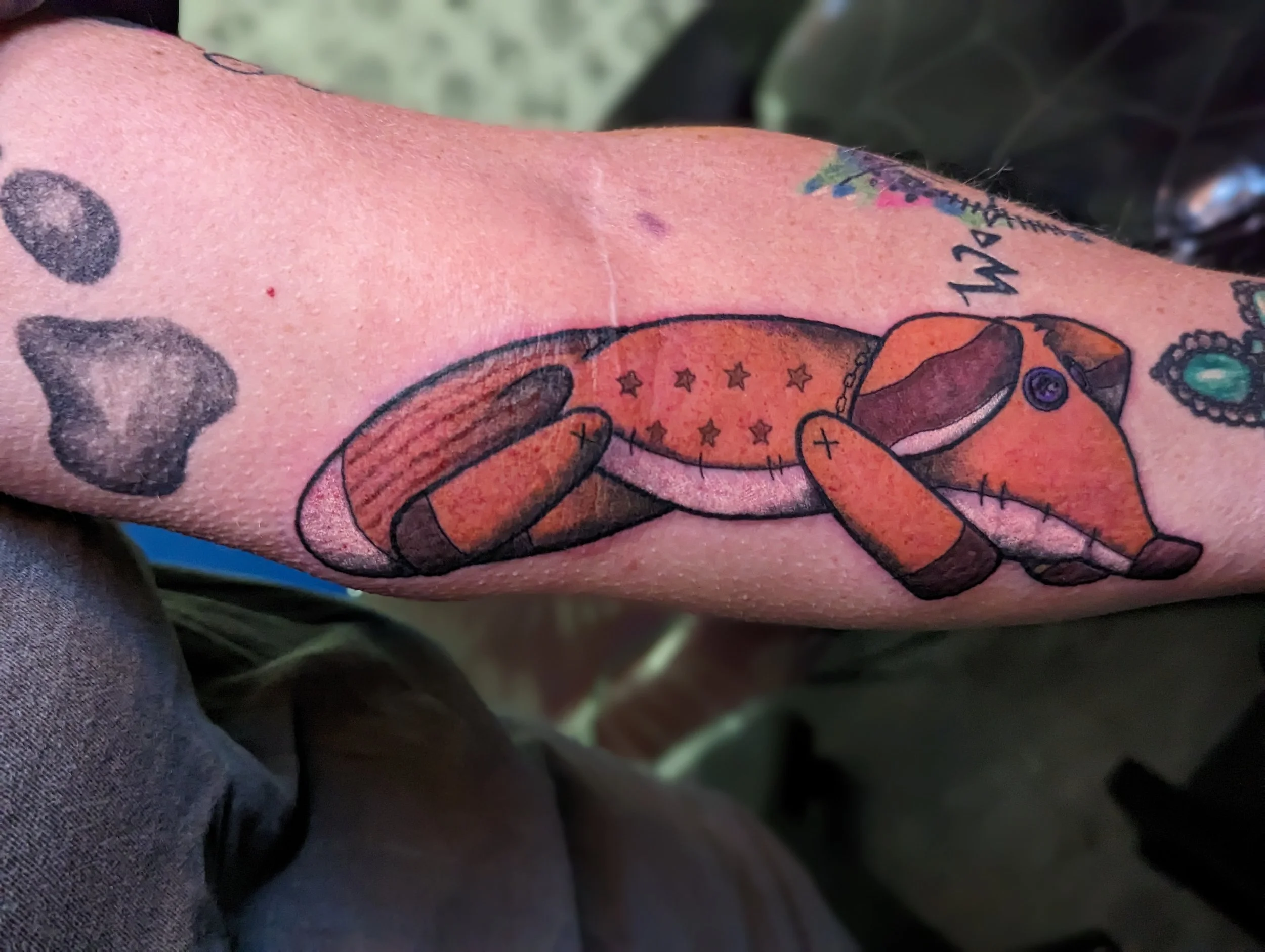 Close-up of a person's arm with colorful tattoos including a cartoon-like bunny and other characters.