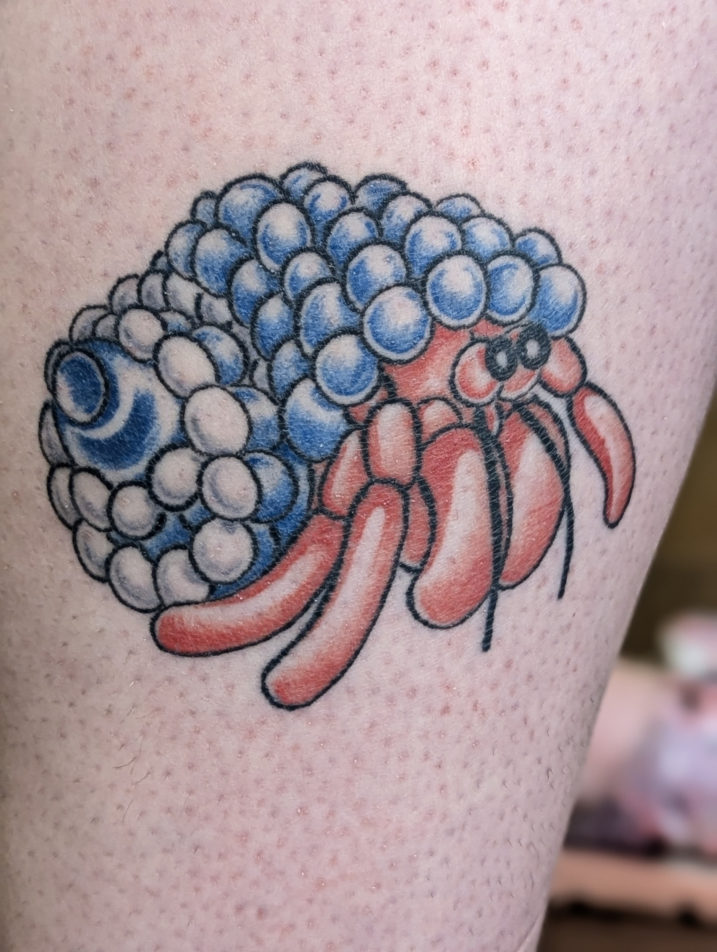 Close-up of a tattoo of a stylized hedgehog with a red tongue and blue spikes, on light skin.