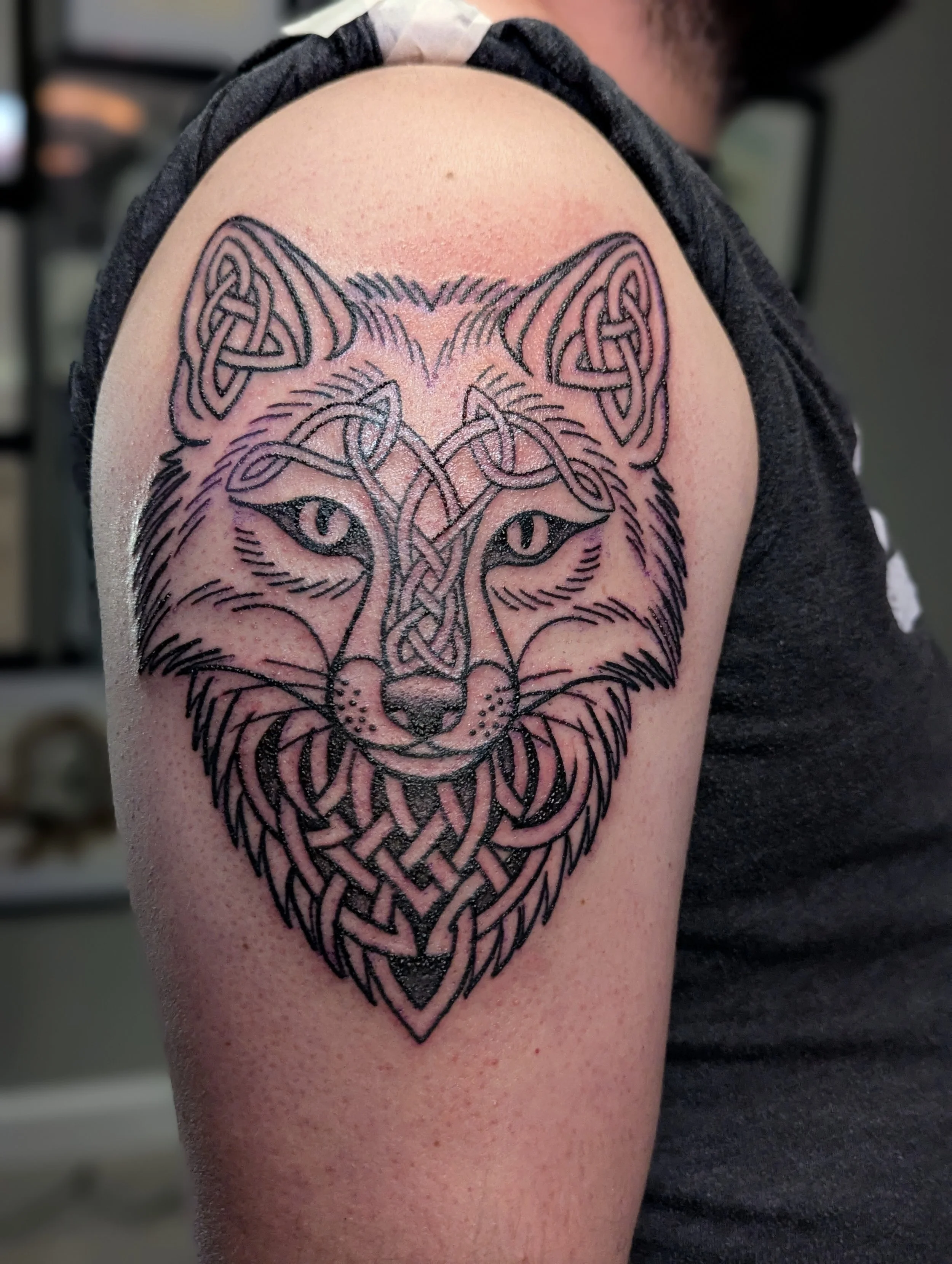 Tattoo of a wolf's face with intricate Celtic knot patterns on a person's upper arm.