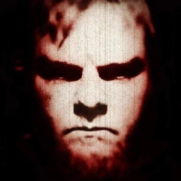 A dark, intense portrait of a man with a stern expression, rendered in high contrast with shadows emphasizing facial features.