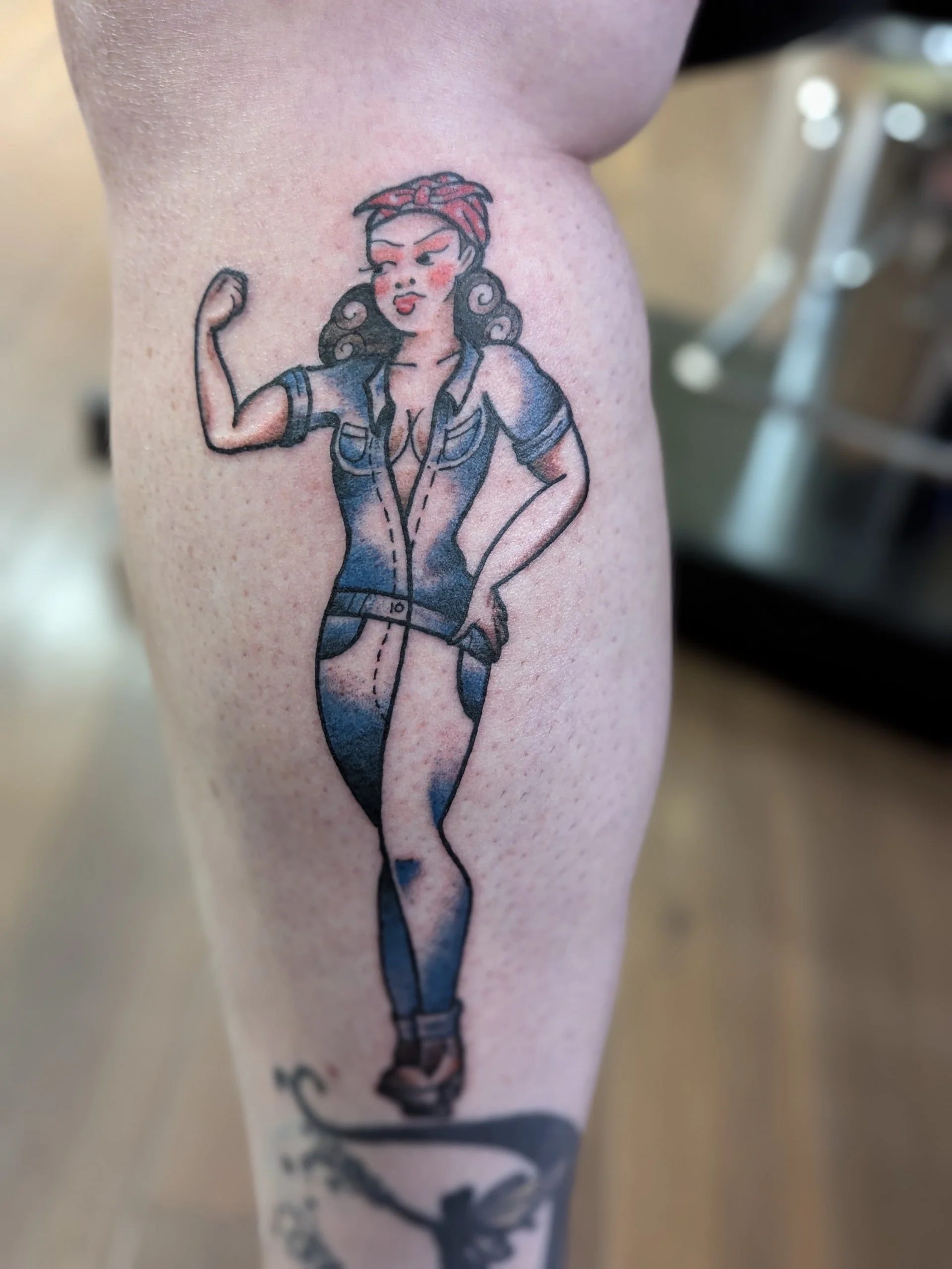 Tattoo of a woman with curly hair, wearing a red bandana and a blue shirt, flexing her arm.