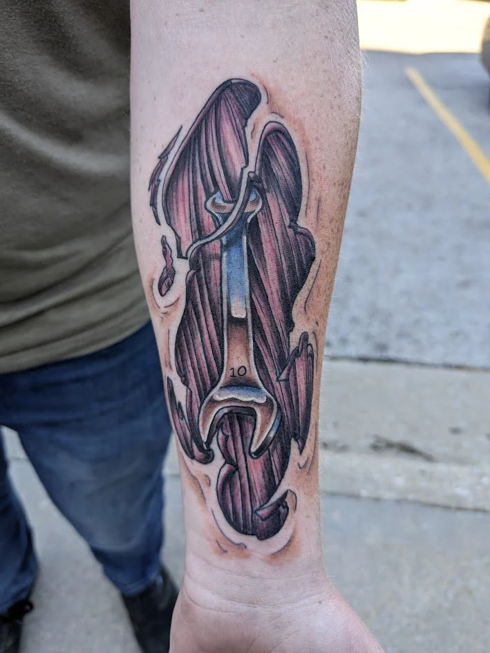 Tattoo of a hammer and sickle with wings on a person's inner forearm.