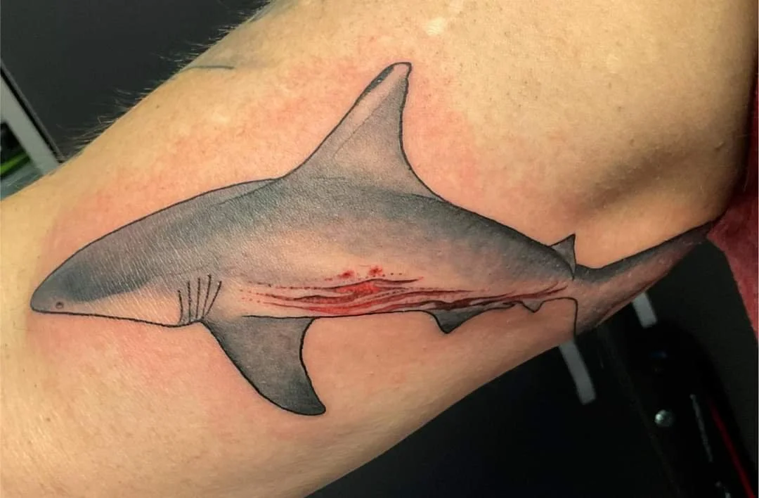 Tattoo of a great white shark on an arm, with red lines inside to resemble wounds.