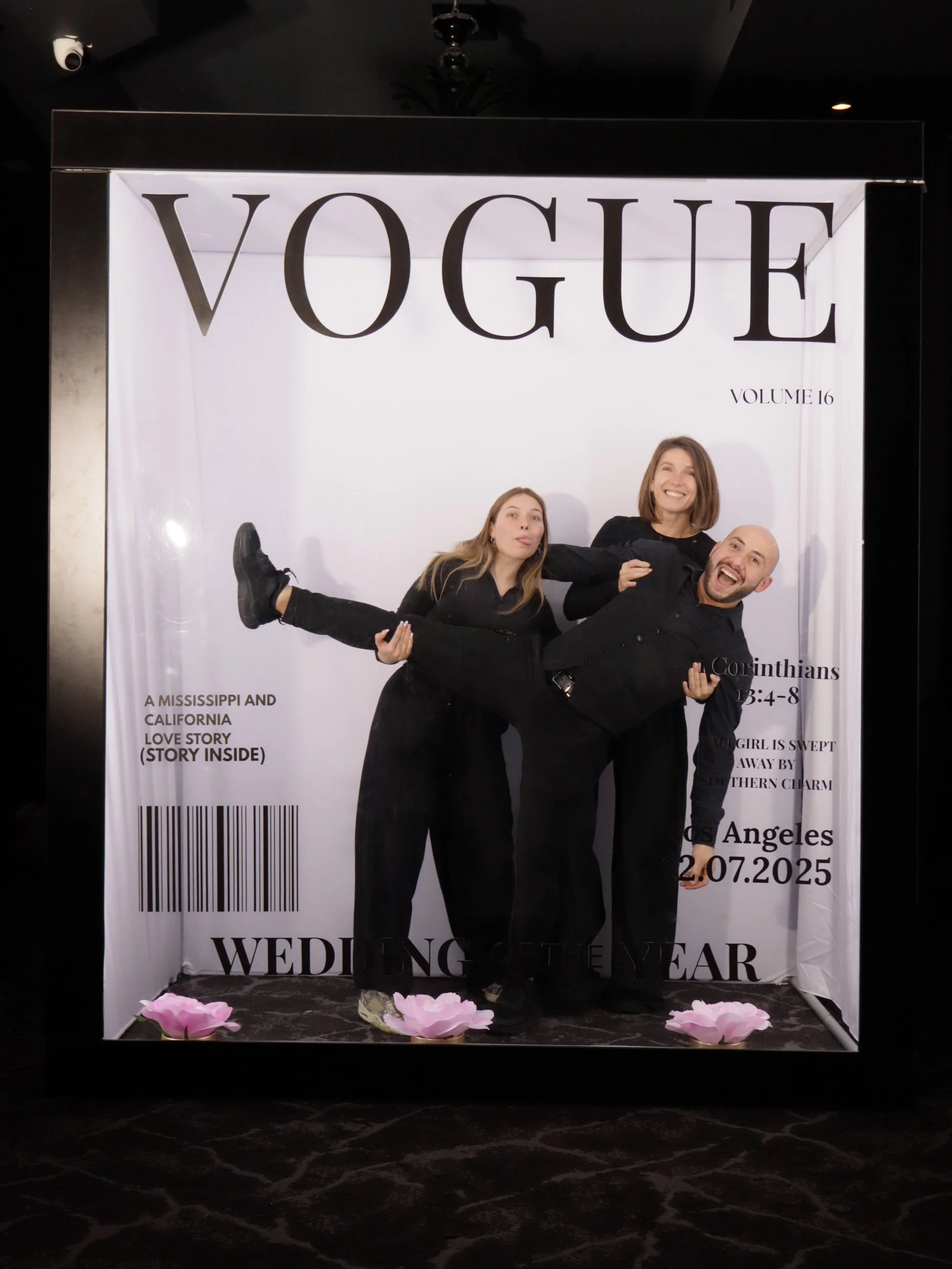 People posing inside a giant Vogue magazine cover frame, with some pink flowers on the floor.