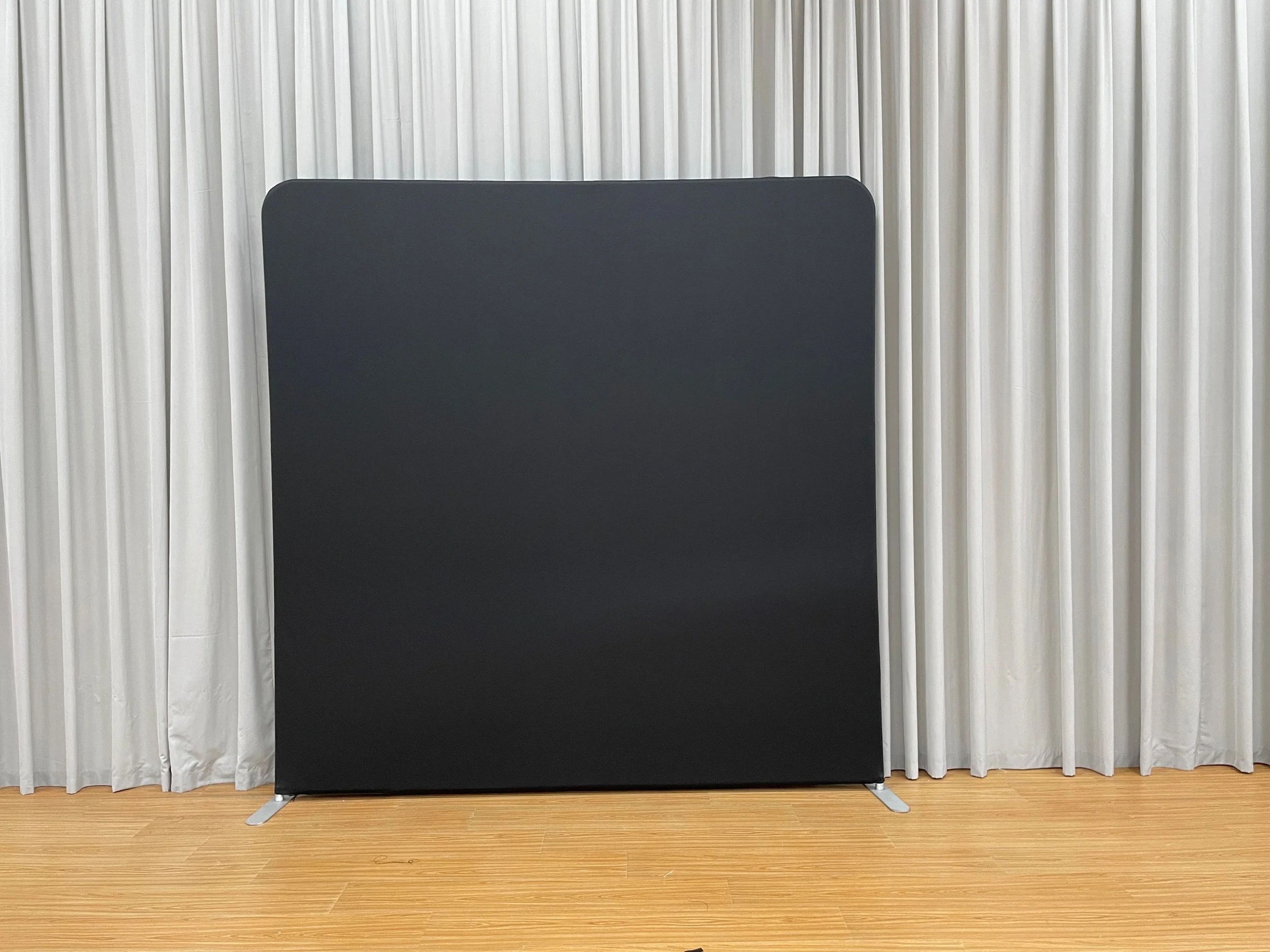 Black partition screen in front of white curtains on wooden floor.