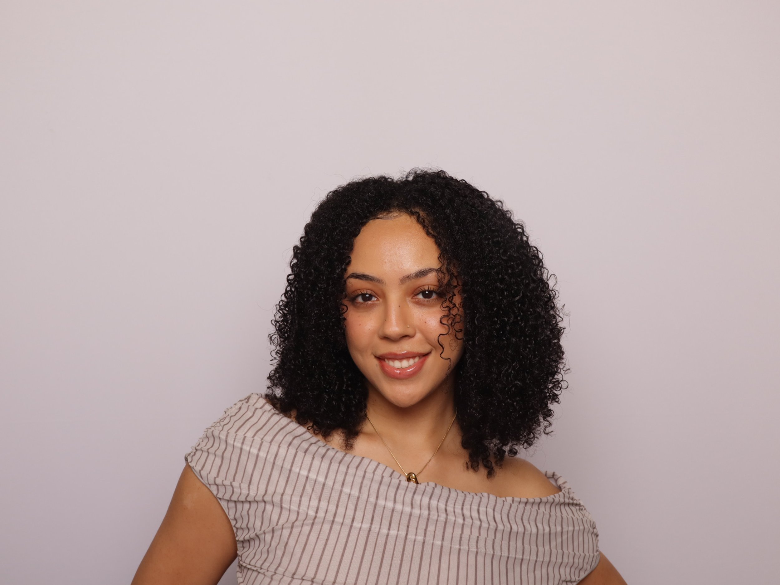 Young woman with curly black hair smiling against a plain white background.