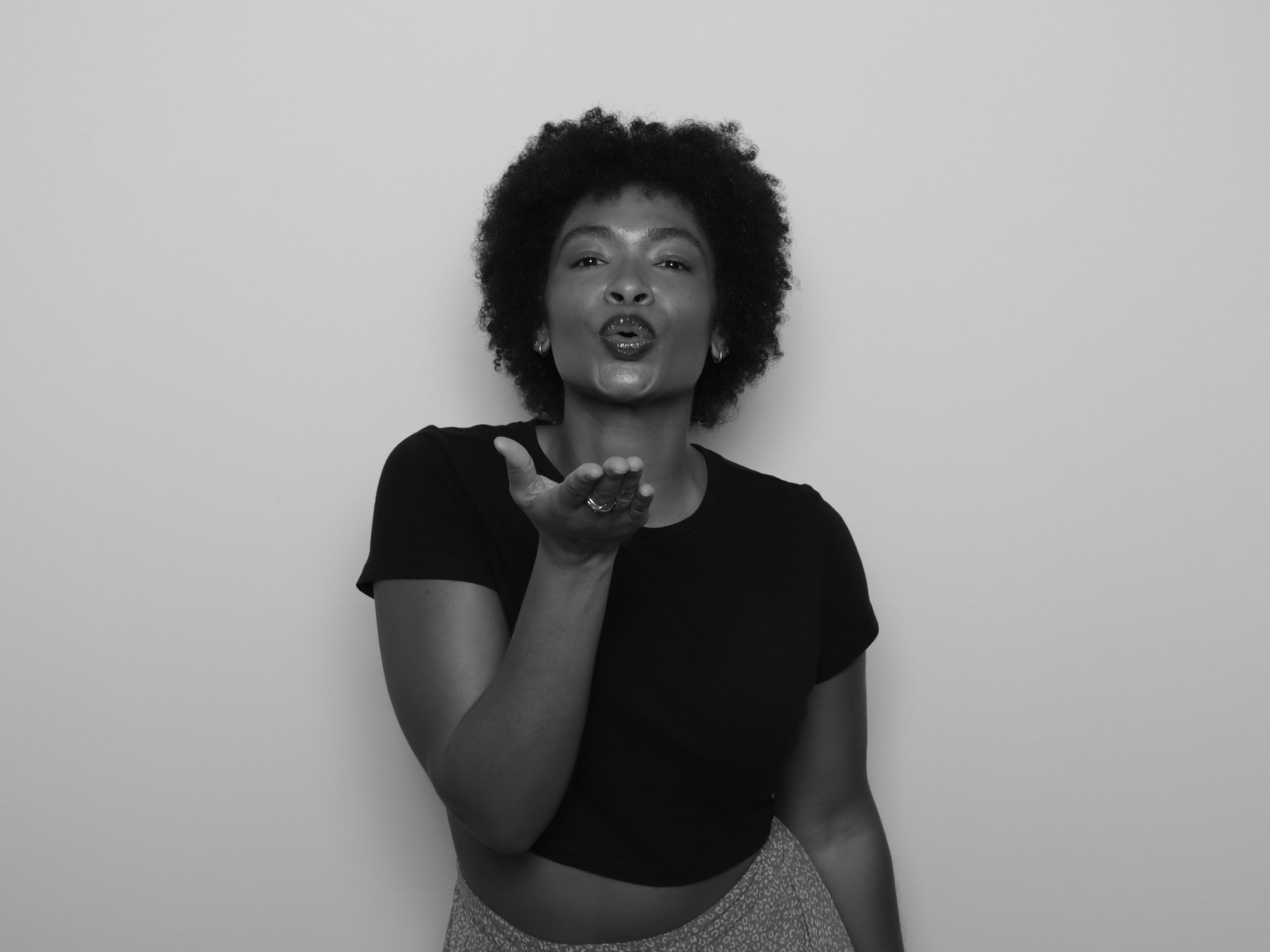 Black and white photo of a woman with curly hair blowing a kiss toward the camera.