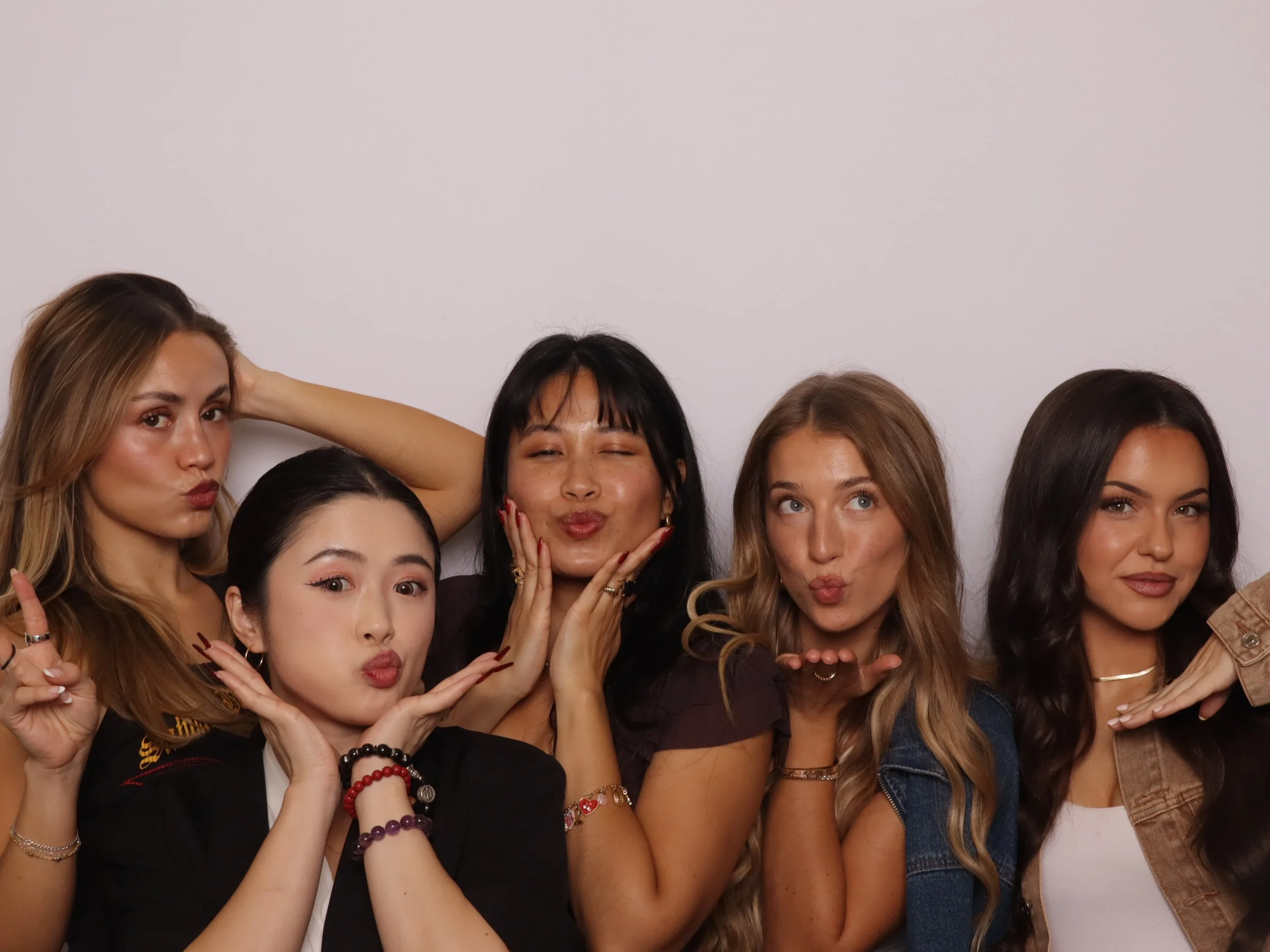 Group of five women posing together and making playful facial expressions against a plain white background.
