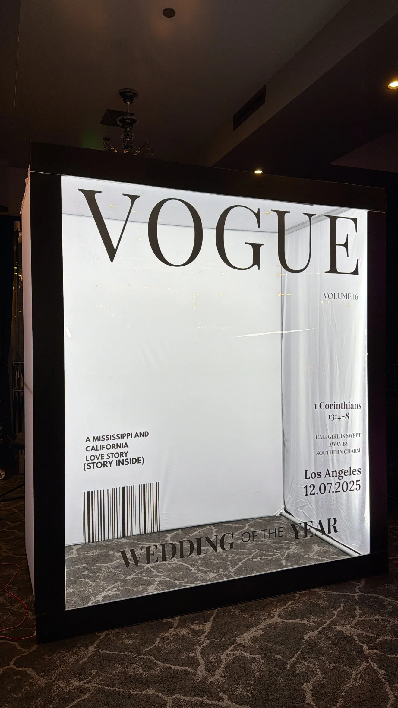 Illuminated display board resembling a magazine cover for Vogue, featuring a wedding announcement with details about a wedding in Los Angeles on July 12, 2025, also includes a barcode and references to a love story from Mississippi and California.