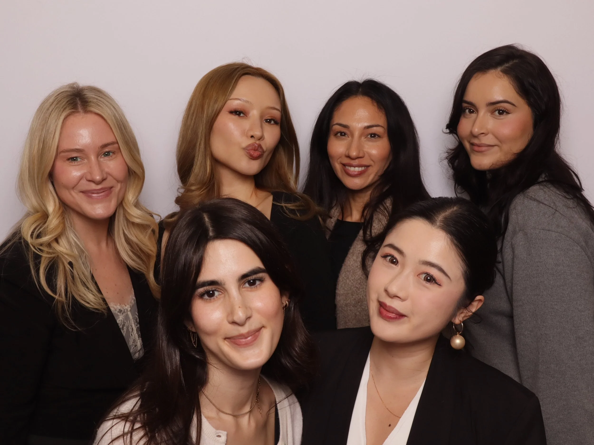 Group of seven women smiling and posing for a photo against a plain white background.