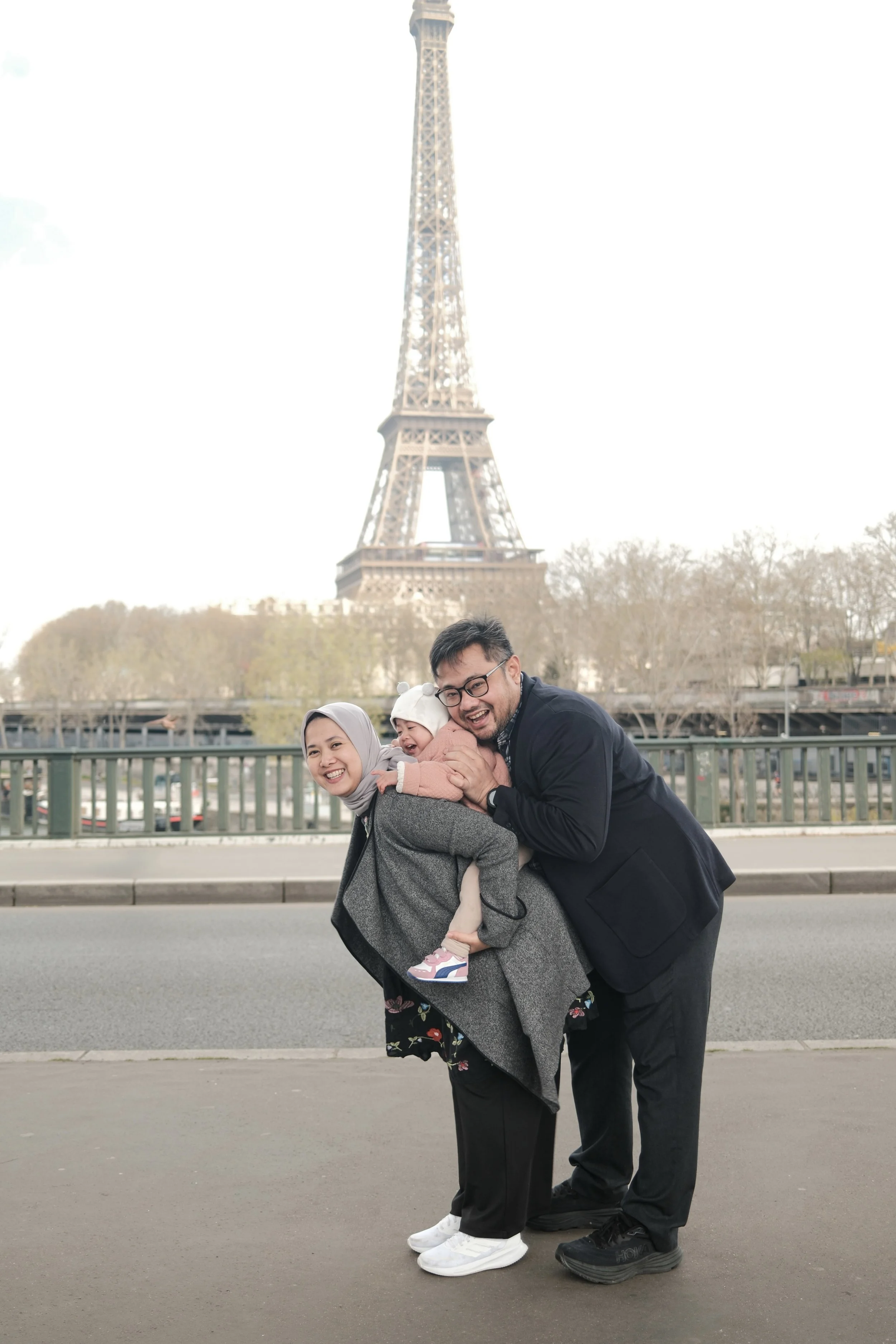 Family of three smiling and playing in front of Eiffel Tower in Paris, France.