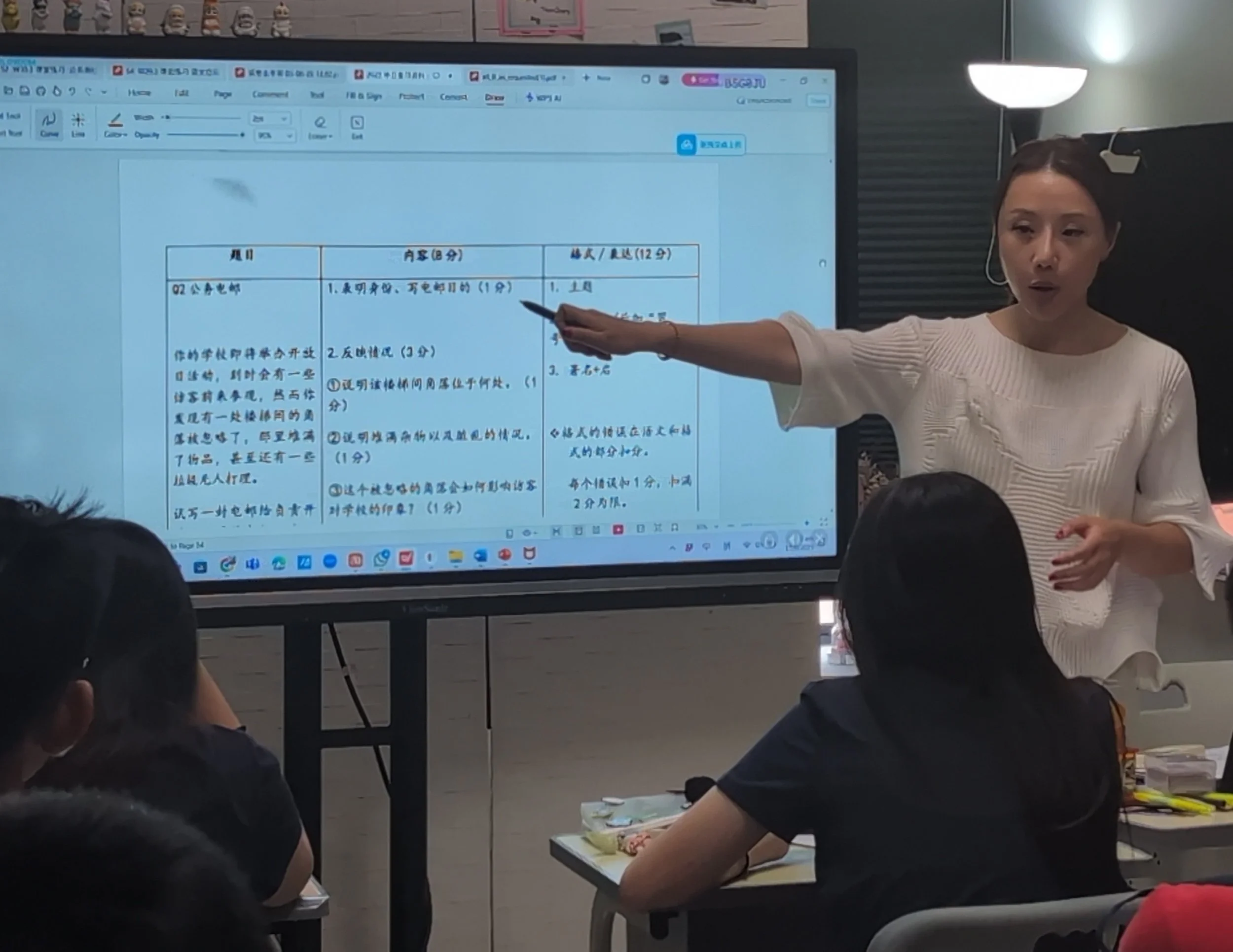 A woman in a white sweater points at a large digital screen displaying a document with Chinese text to a group of students in a classroom setting.
