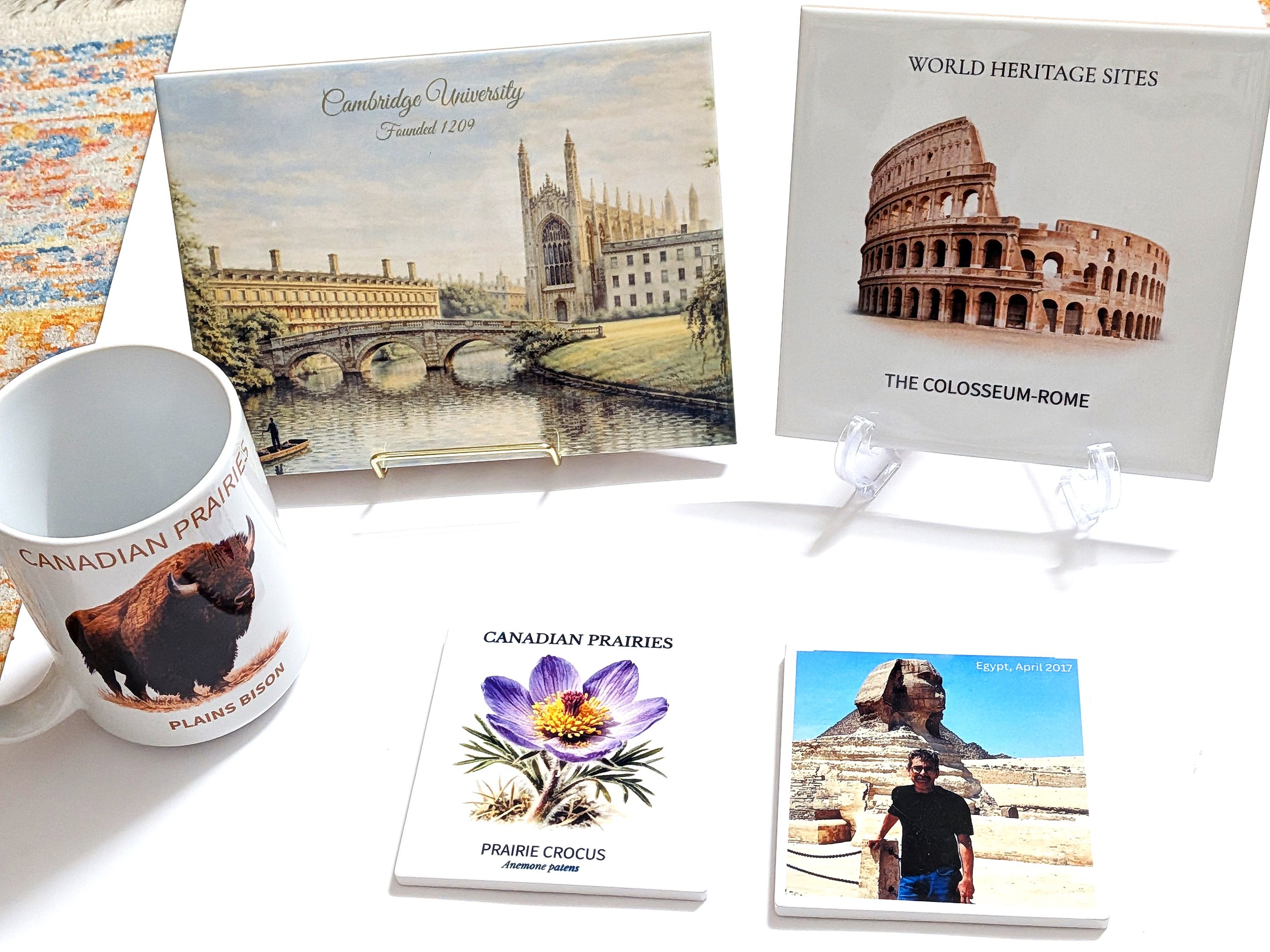Collection of souvenirs including a mug with a bison and Canadian prairie scene, ceramic tiles of famous world heritage sites the Colosseum and Cambridge University, a card of Prairie Crocus flower, and a photograph of a man at the pyramids of Egypt.