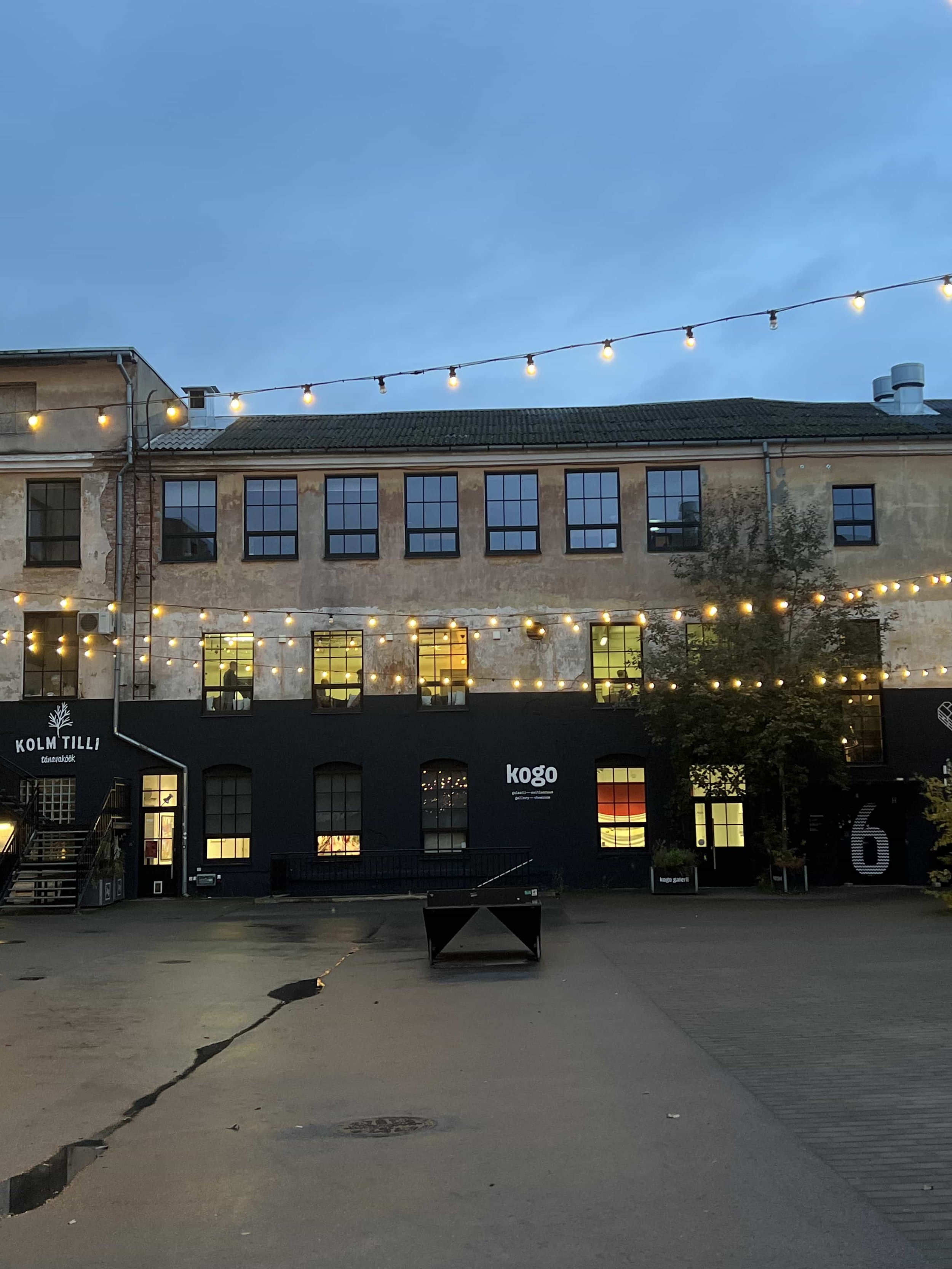 Aparaaditehase hoone Tartus õhtutuledes. Kollased valgusread hoovi kohal, akendest paistab soe valgus. Hoones asub Mind & Motion heaolustuudio.