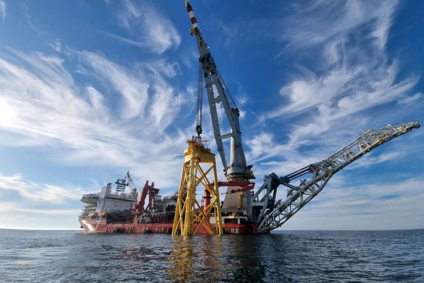 An offshore oil drilling rig in the ocean with a blue sky and scattered clouds above.