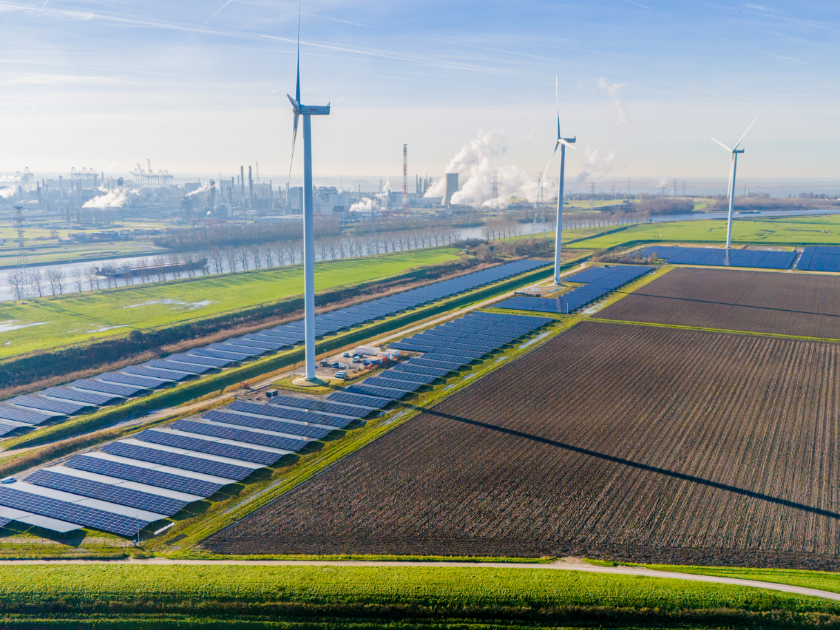 Aerial view of solar panels and wind turbines in a rural landscape.