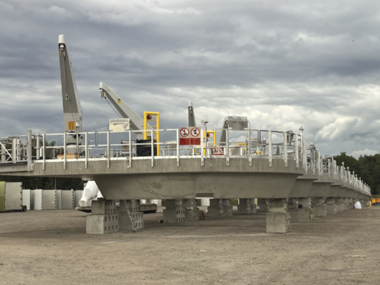 Large commercial floating platform reinforced with concrete blocks, with warning signs and industrial equipment, set against a cloudy sky.