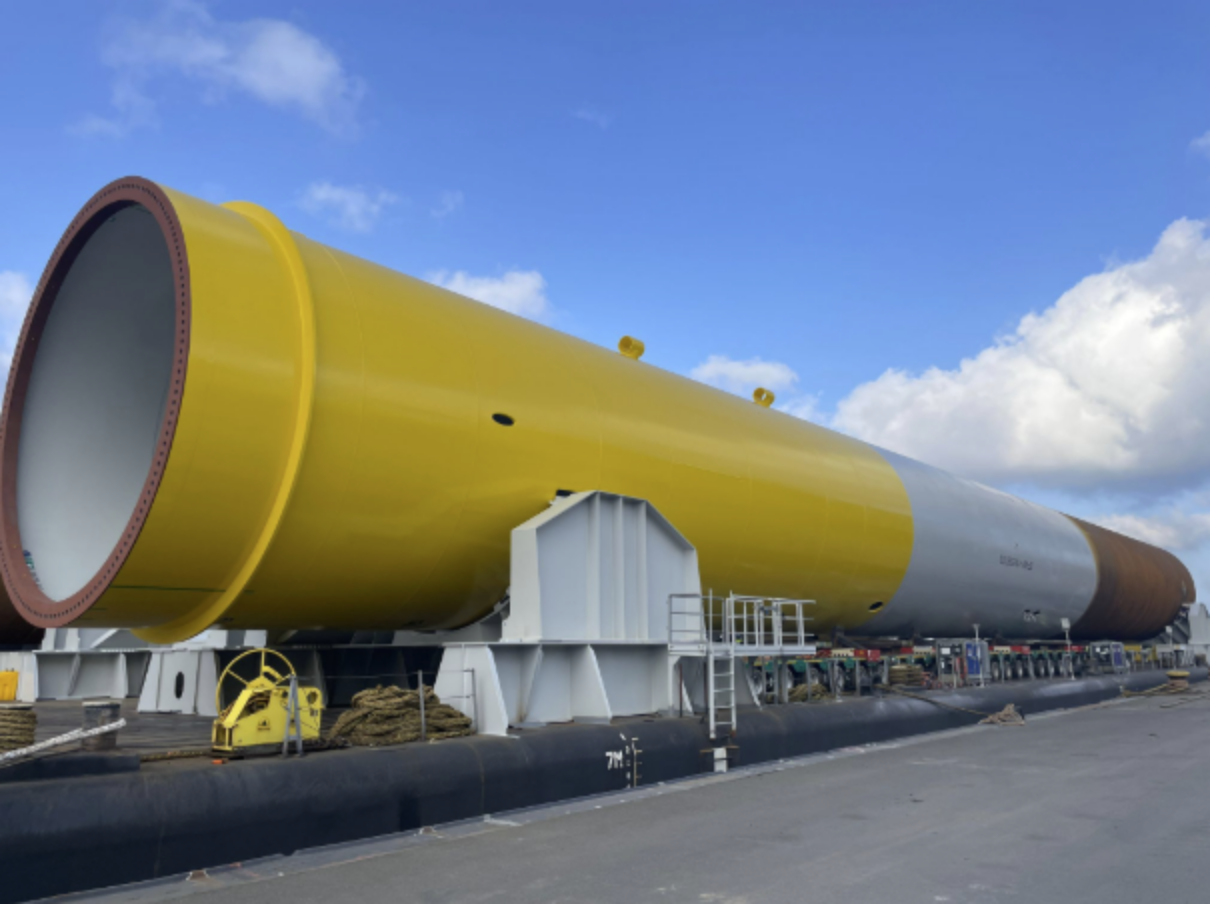 A large cylindrical object, painted yellow and gray, lying on a flatbed trailer on a road.