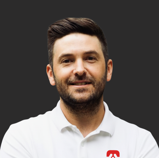 Sean wearing a white collared shirt with a logo on the chest, against a dark background.