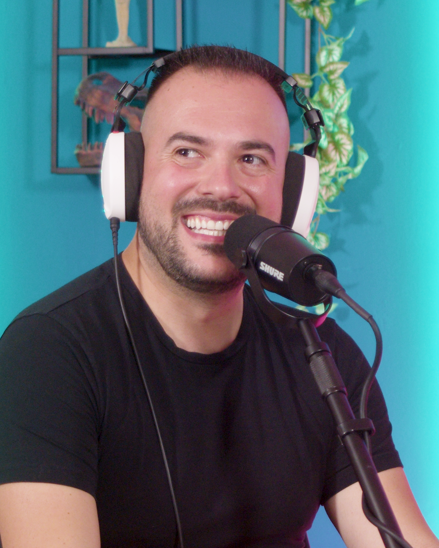 Uomo sorridente con cuffie e microfono in un ambiente colorato.