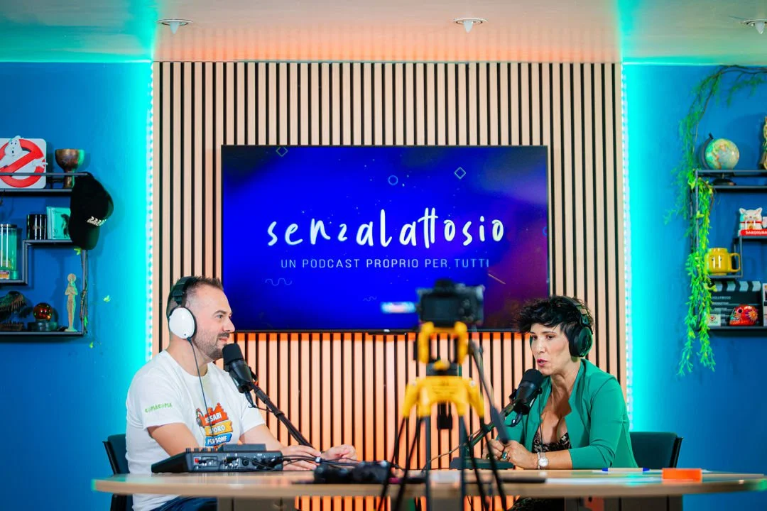  due persone che registrano un podcast in uno studio, con pannelli in legno sullo sfondo e uno schermo con scritto 'Senzalattasio - un podcast proprio per tutti'