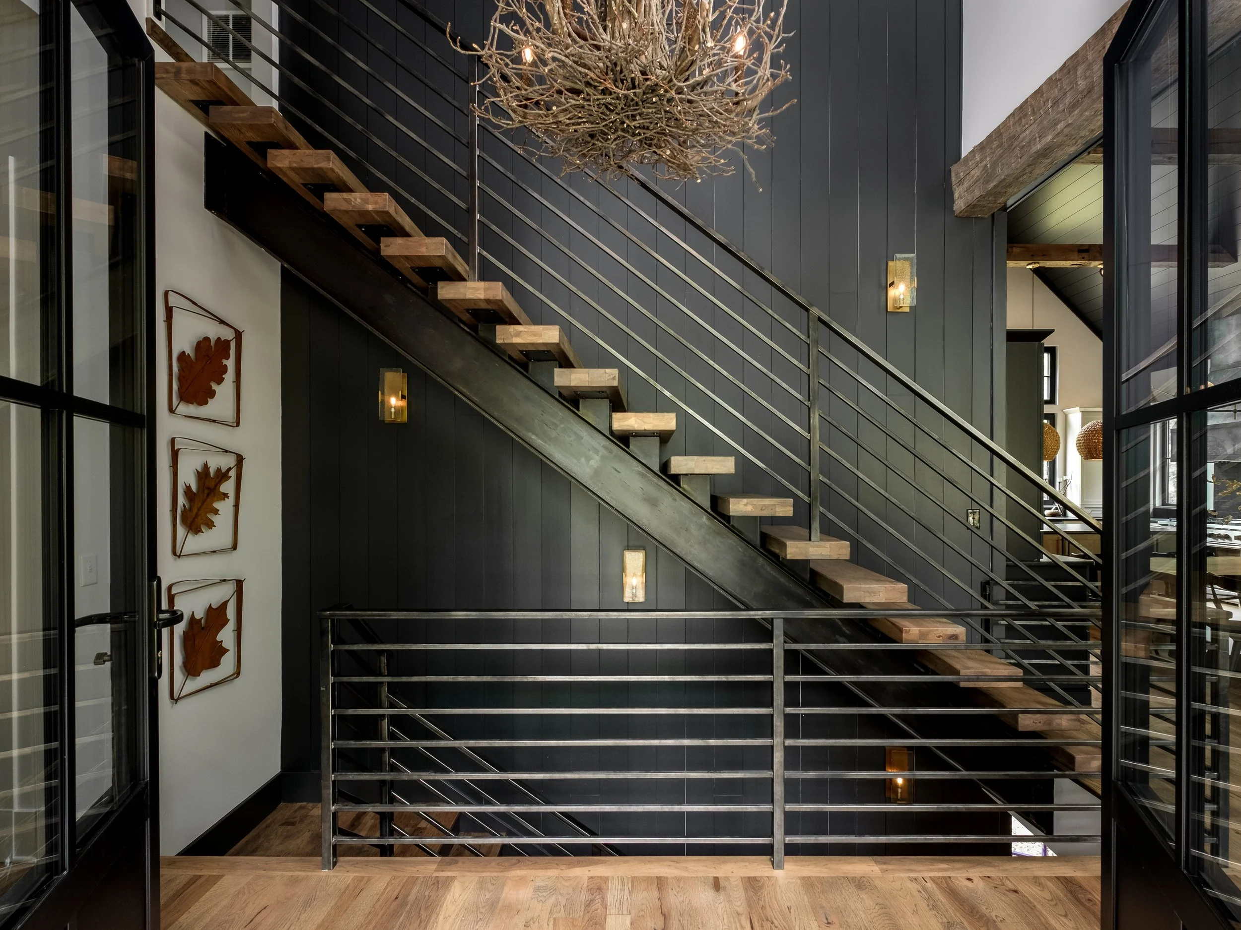 Interior view of a modern staircase with wooden steps and black metal railings, leading to an upper floor in a house with dark walls and decorative wall art.