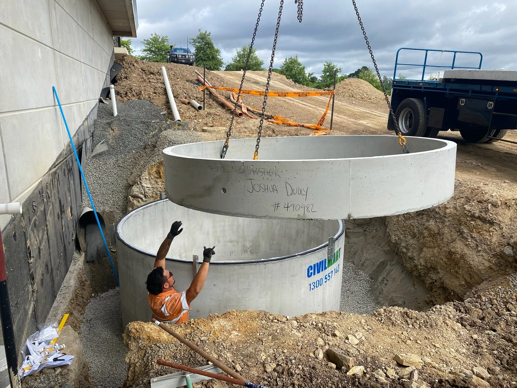 Construction worker in orange safety vest and gloves installing large concrete pipes at a construction site