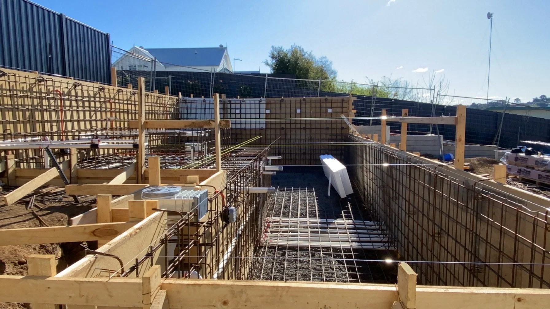 Construction site with wooden framing and steel rebar for concrete foundation, under bright sunlight.