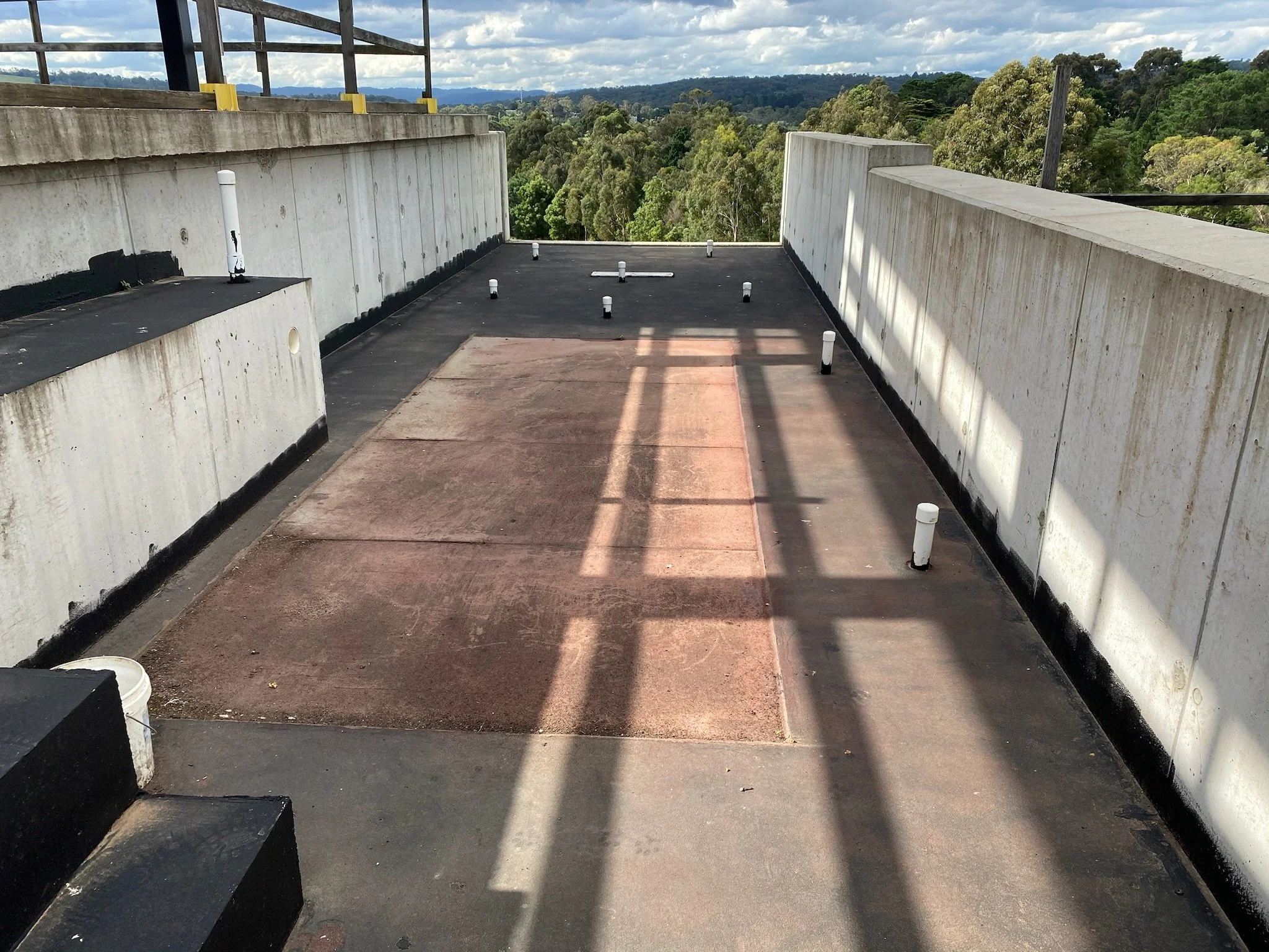 Rooftop with white walls, small pipes, and a view of trees and blue sky in the background.