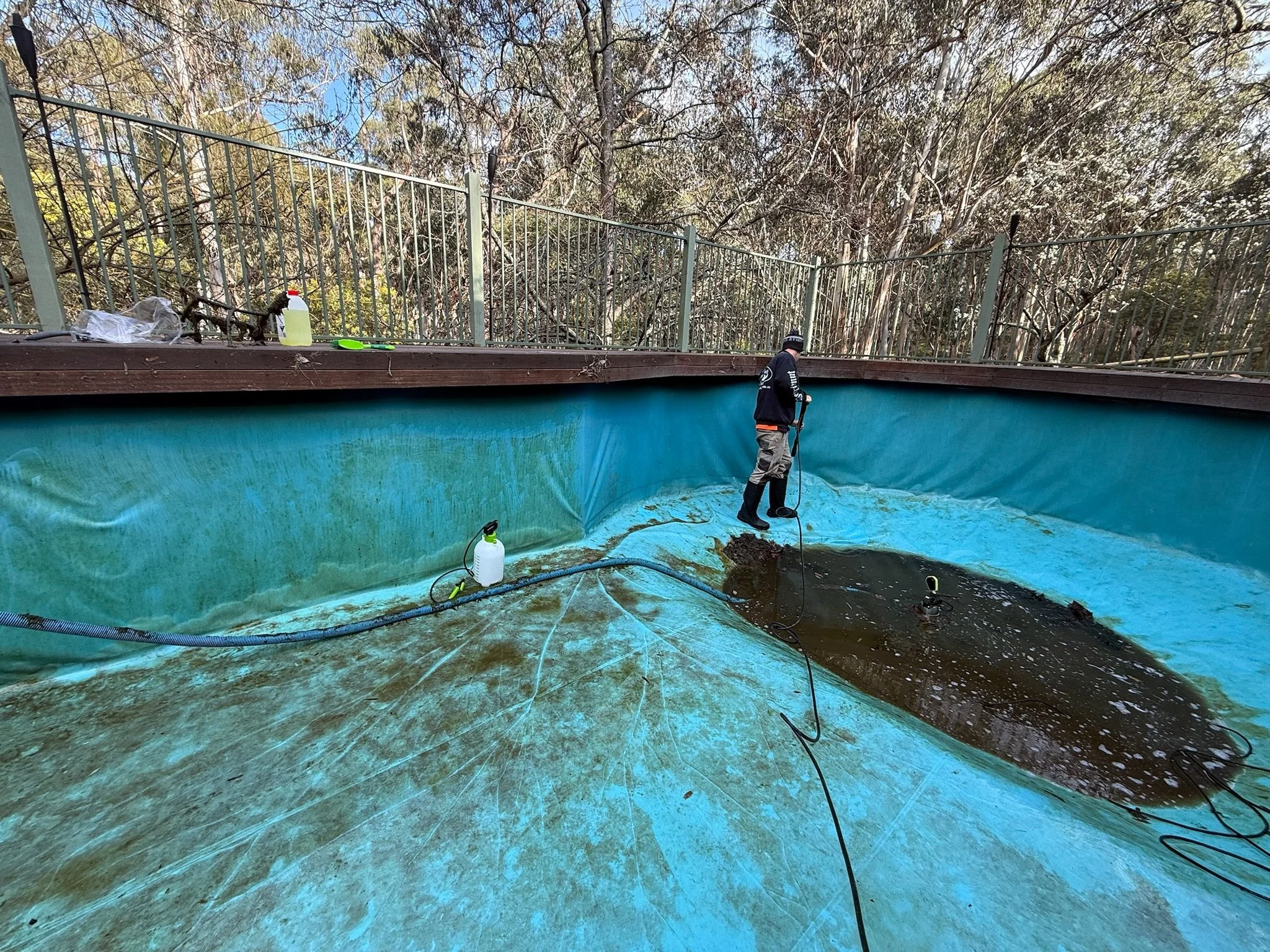 Person cleaning dirt out of a backyard pool with a power washer.