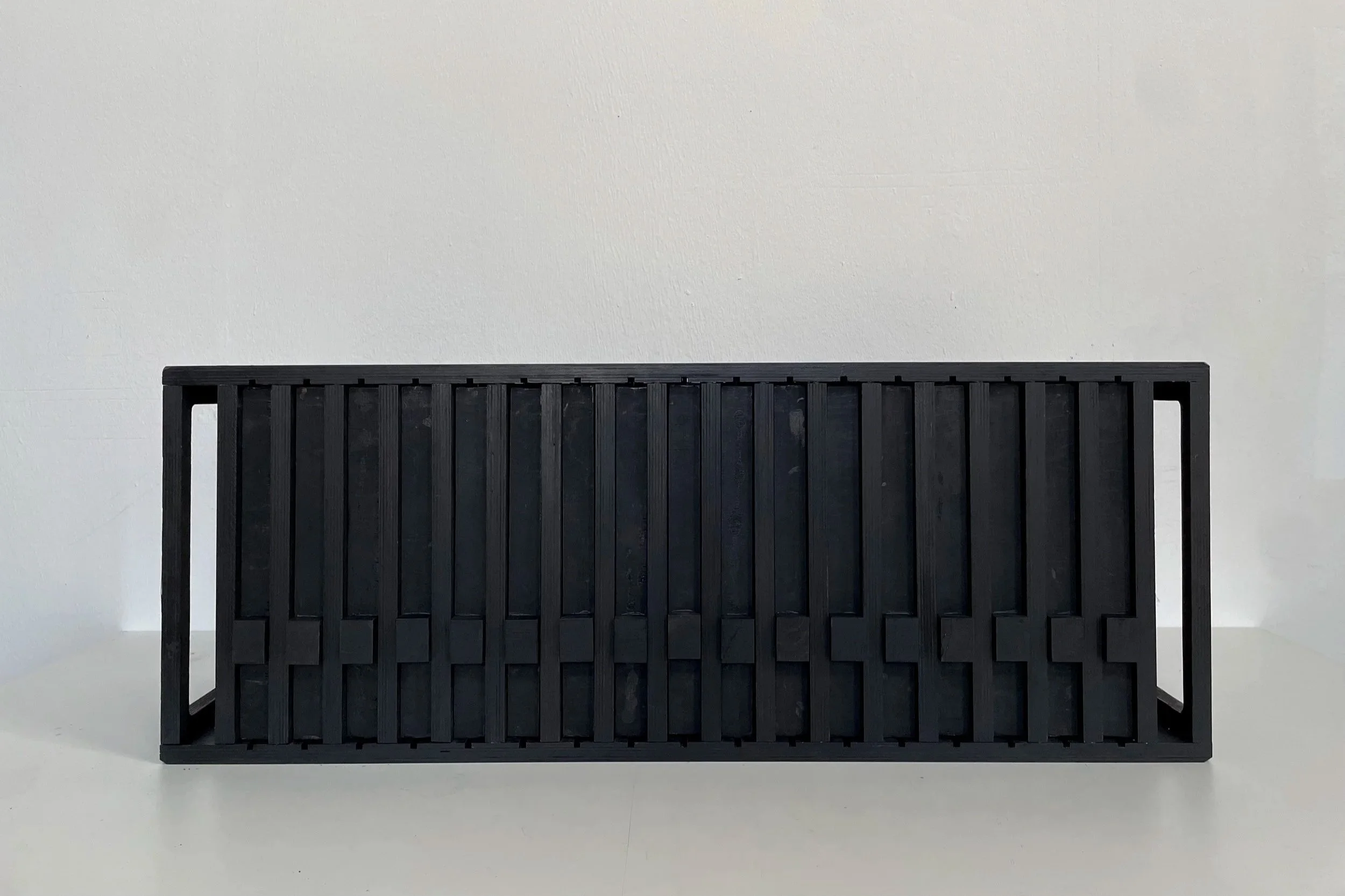 Black wooden frame with vertical slats, placed on a white surface against a white wall.